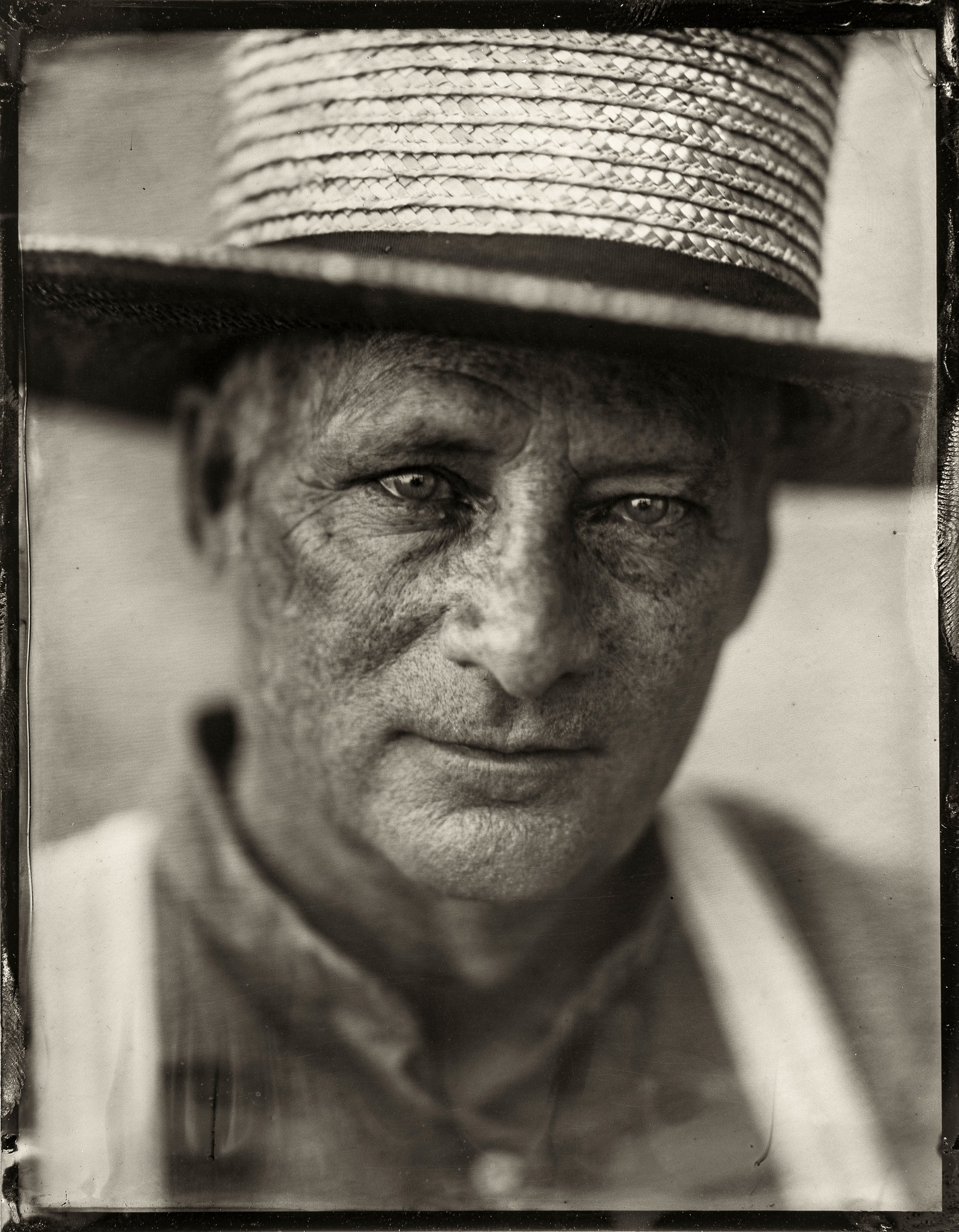 A close-up tintype photograph of a man with piercing eyes and a serious expression, wearing a wide-brimmed straw hat.