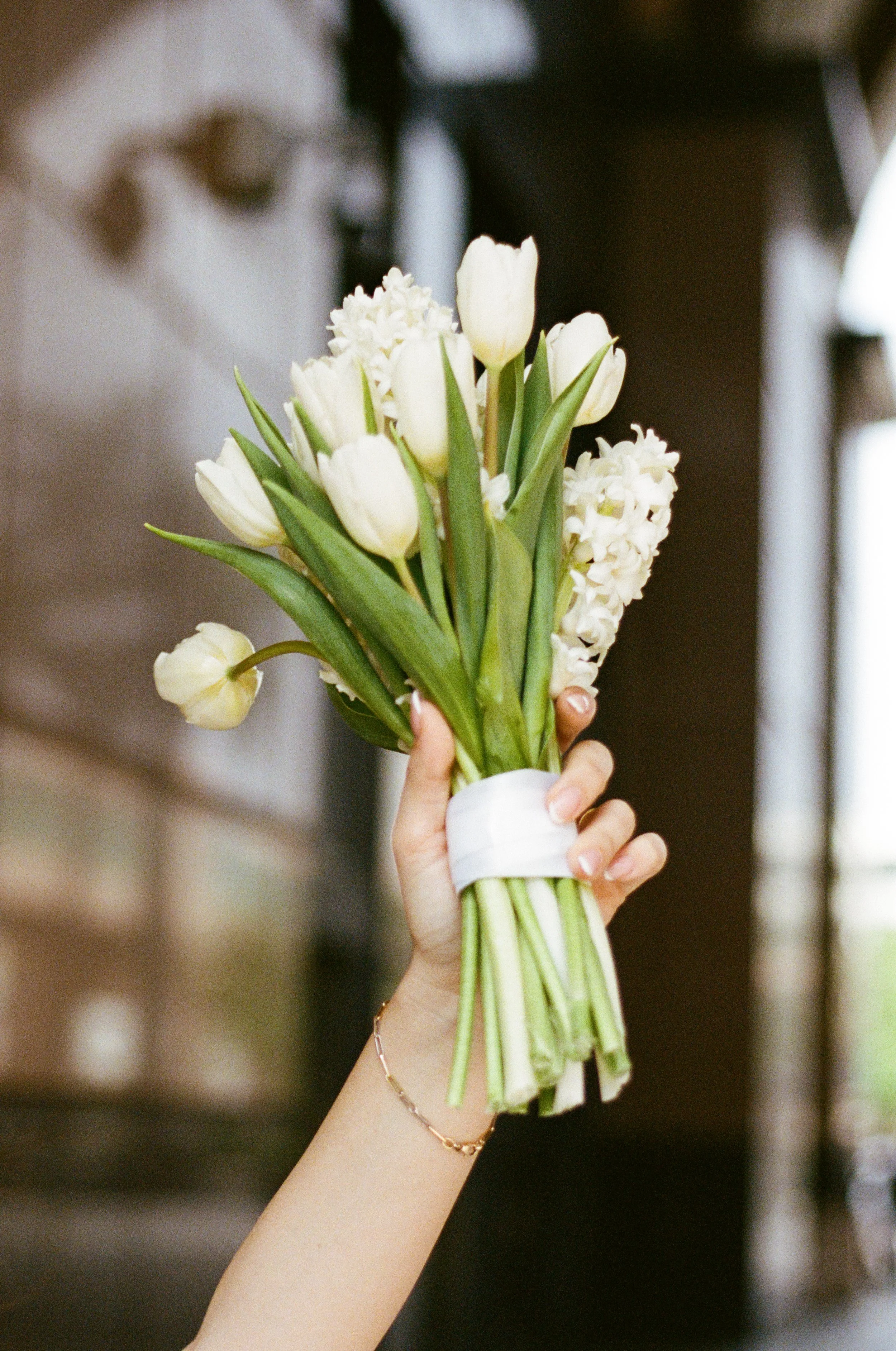 A hand holding a bouquet of white tulips and hyacinths.