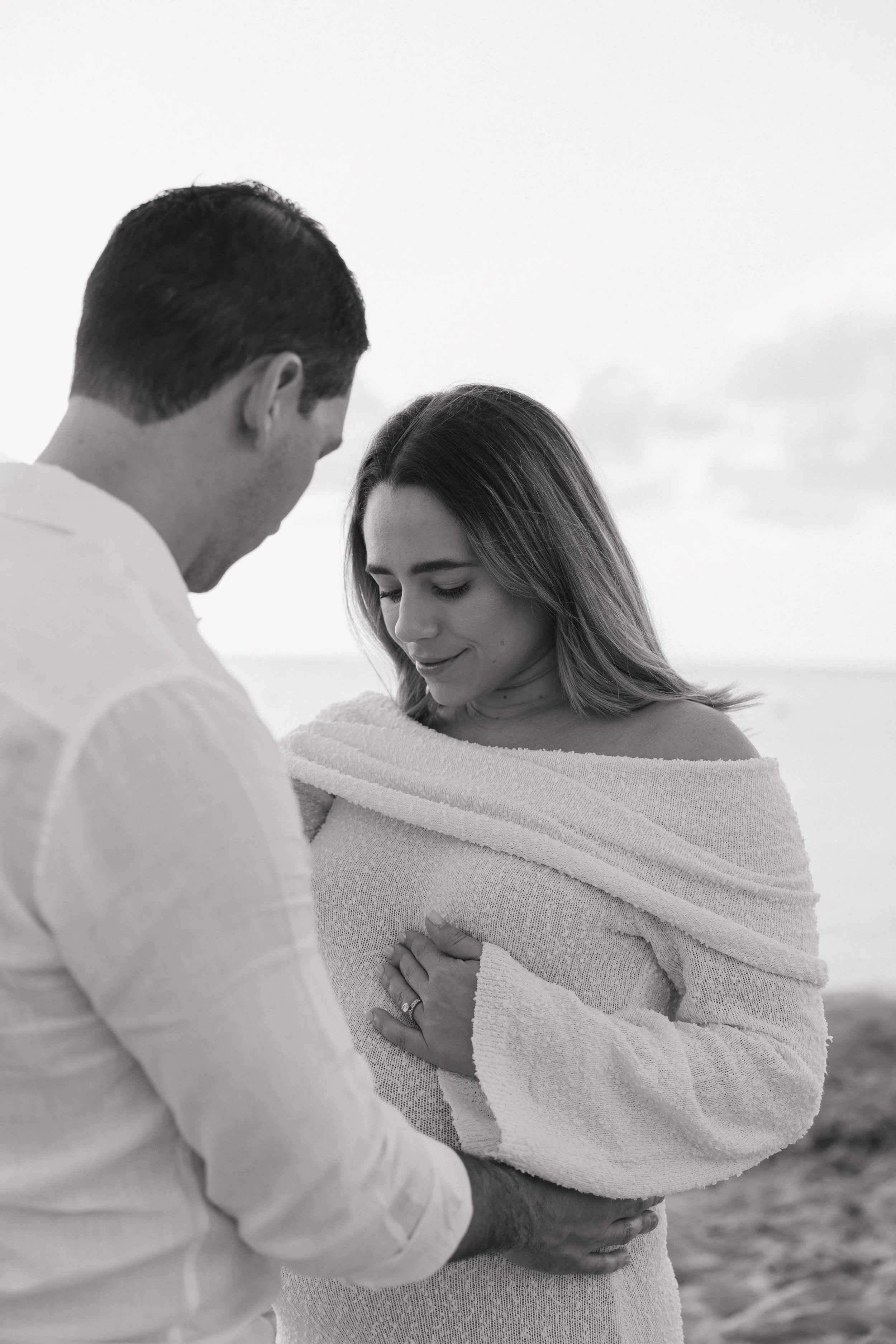 A couple appears to be expecting a baby, with the man cradling the woman's pregnant belly and both smiling gently.