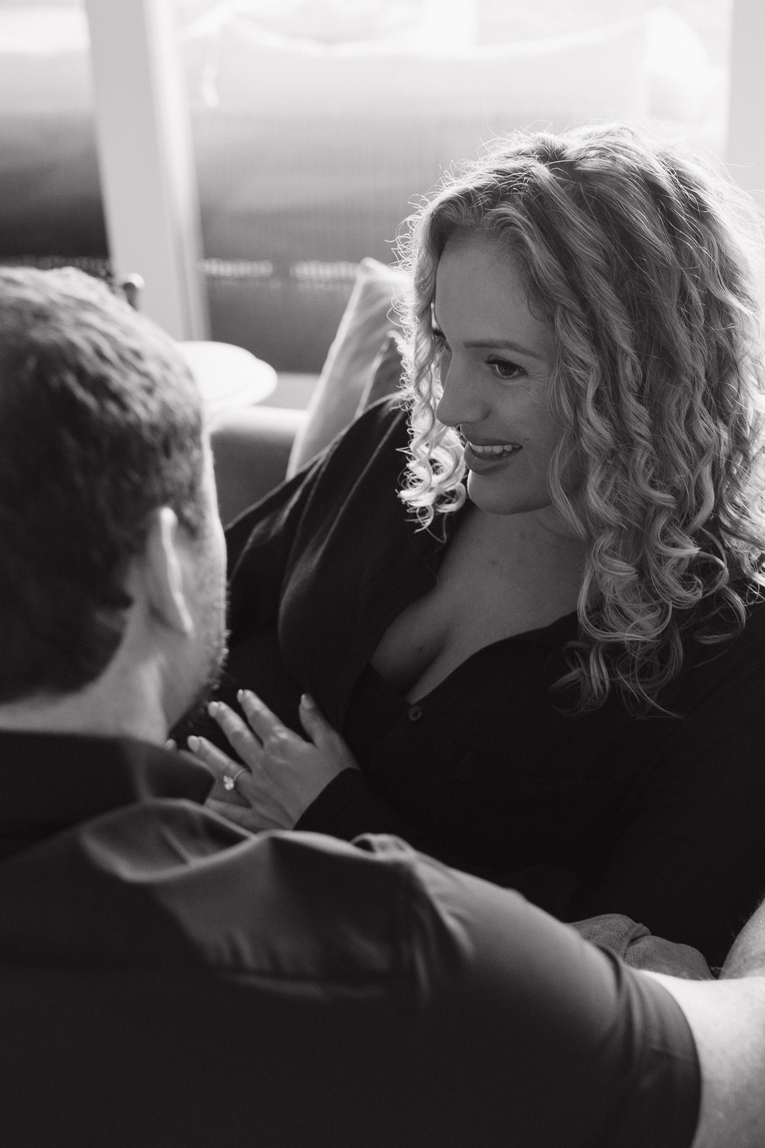 A woman with curly hair smiling and looking at a man, who is holding her hand, in a close-up black-and-white photograph.