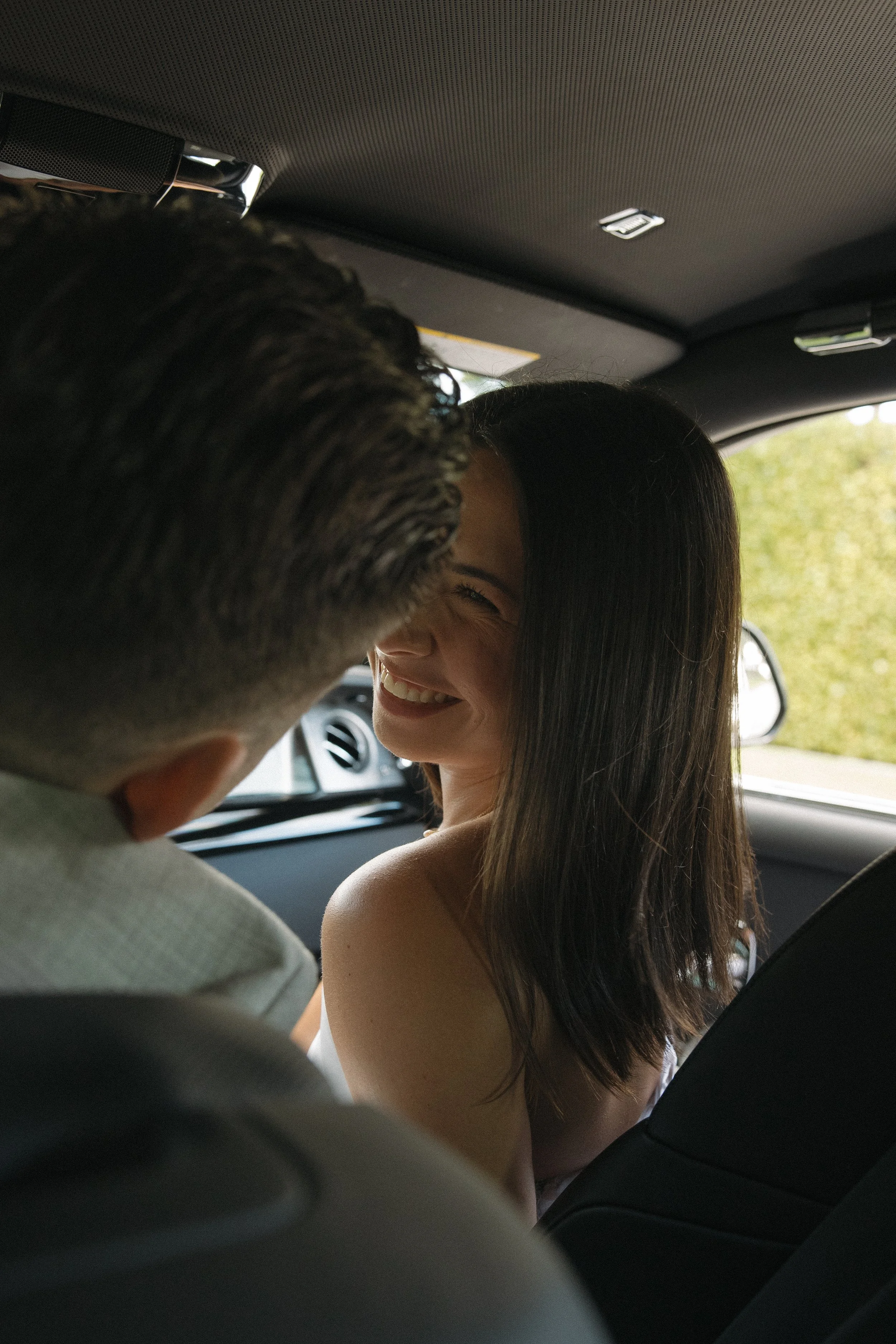 A woman with dark hair smiling and leaning toward a person with short hair, sitting inside a car.