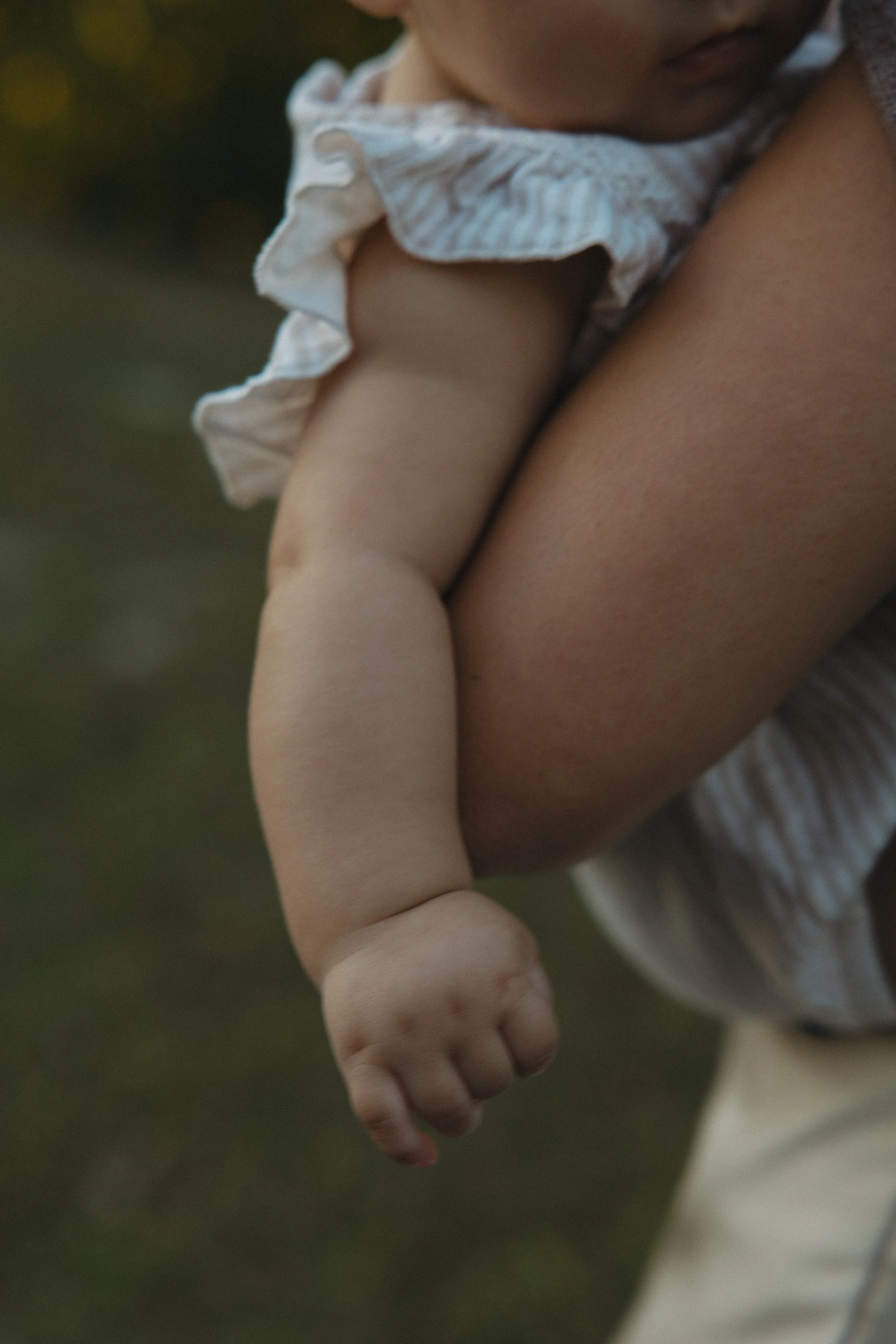 Close-up of a child holding an adult's finger outside, with a blurred background.