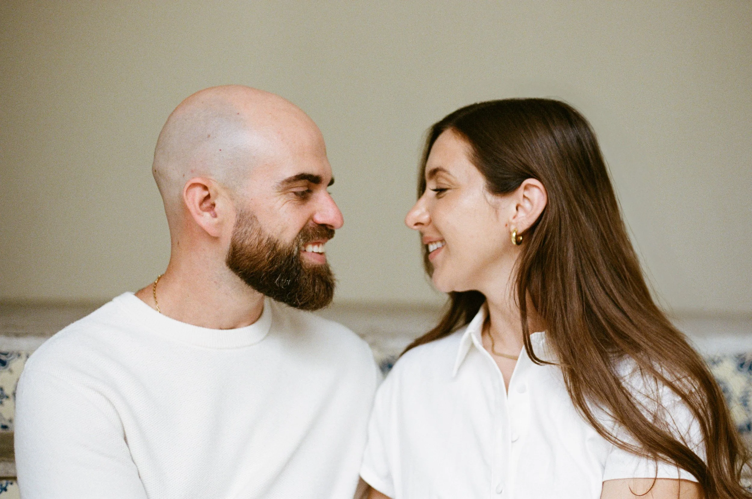 A man with a beard and a woman with long brown hair facing each other closely, smiling softly.