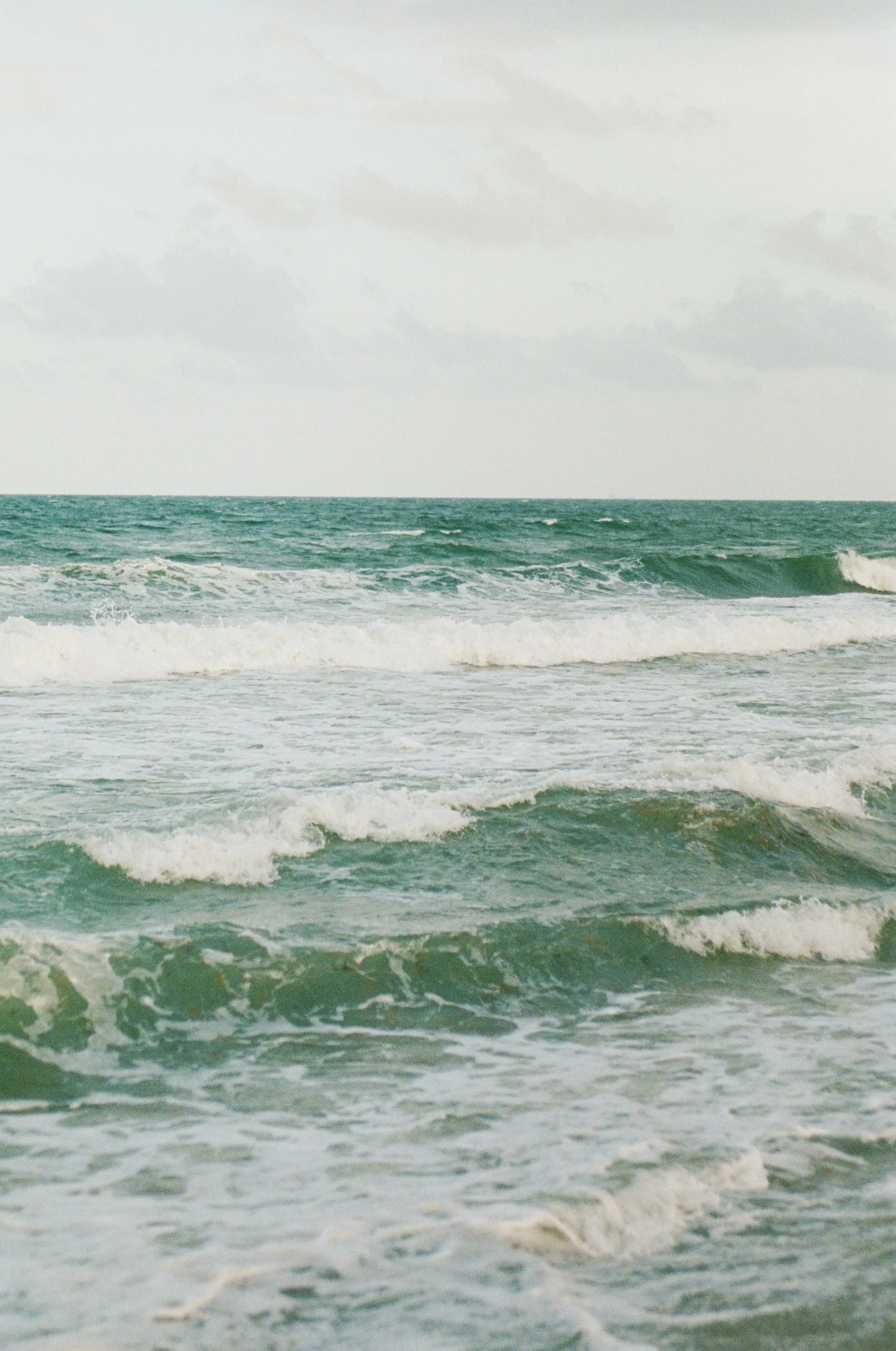 Ocean waves crashing on a sandy beach under a cloudy sky.