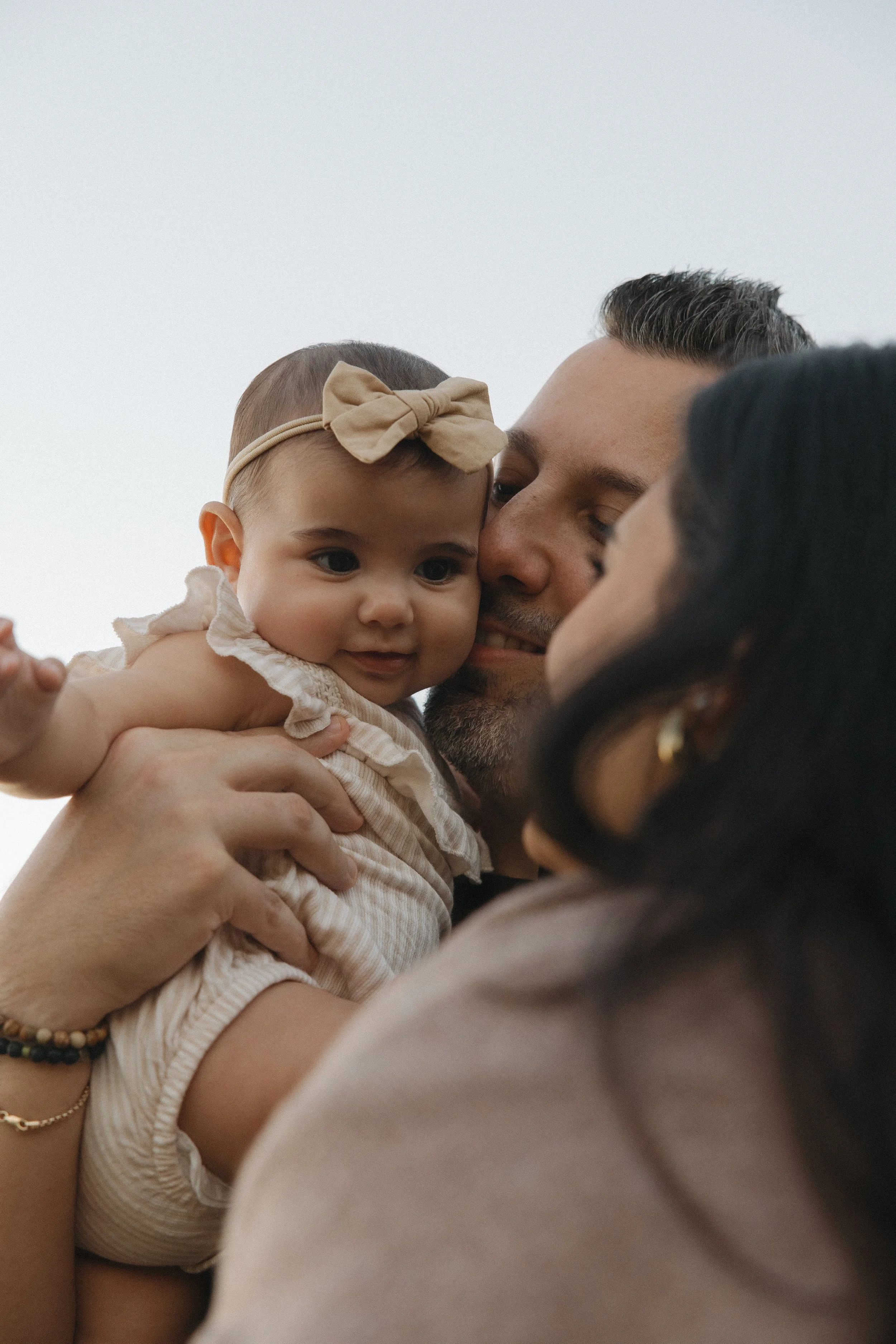 A person holding a young girl with a beige bow headband, close-up of faces as they share a moment of affection.