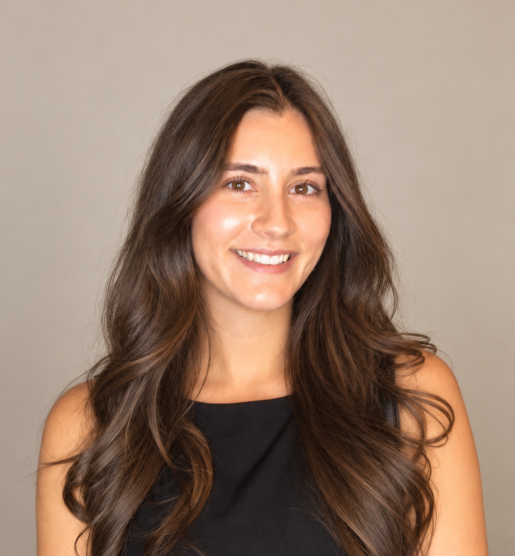 Portrait of a woman with long, wavy brown hair, wearing a black sleeveless top, smiling against a neutral background.