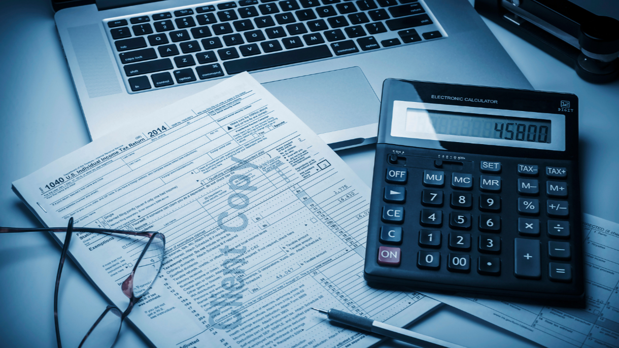 Desk with a laptop, a 2014 U.S. tax form, a pair of glasses, a pen, and a calculator showing 45,800.