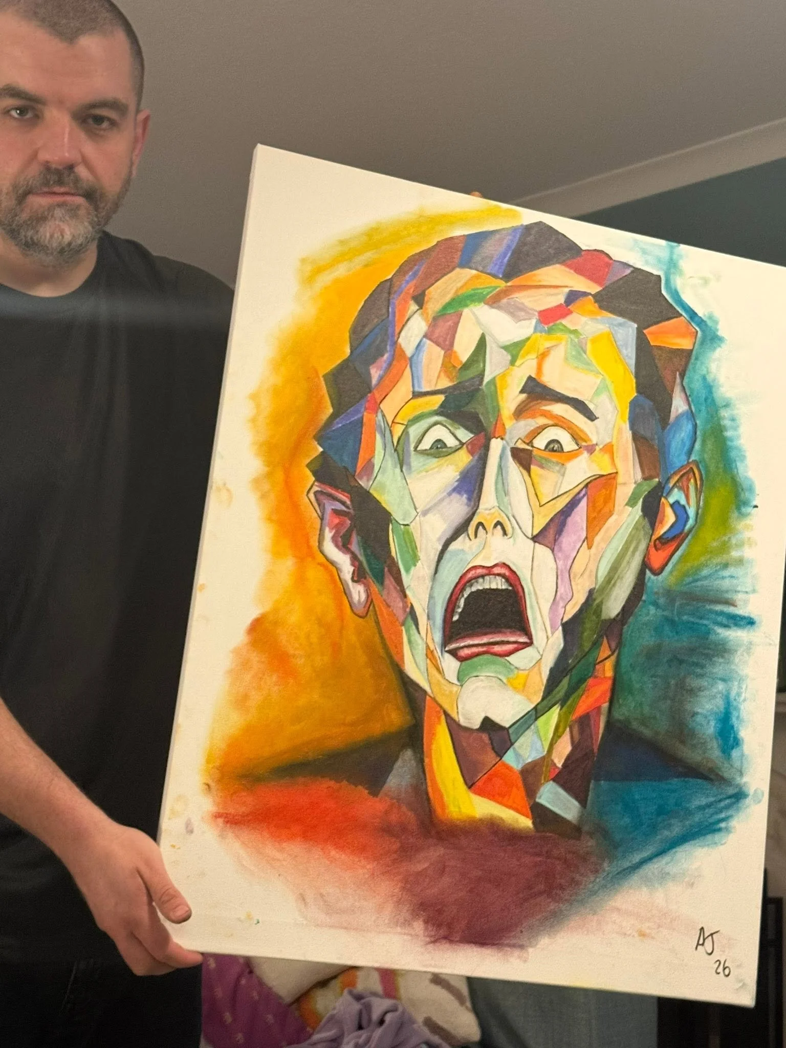 A man with short hair and a beard holding a colorful, abstract portrait painting of a woman's face with surprised or shocked expression, painted in a cubist style, signed with initials and dated 2026.