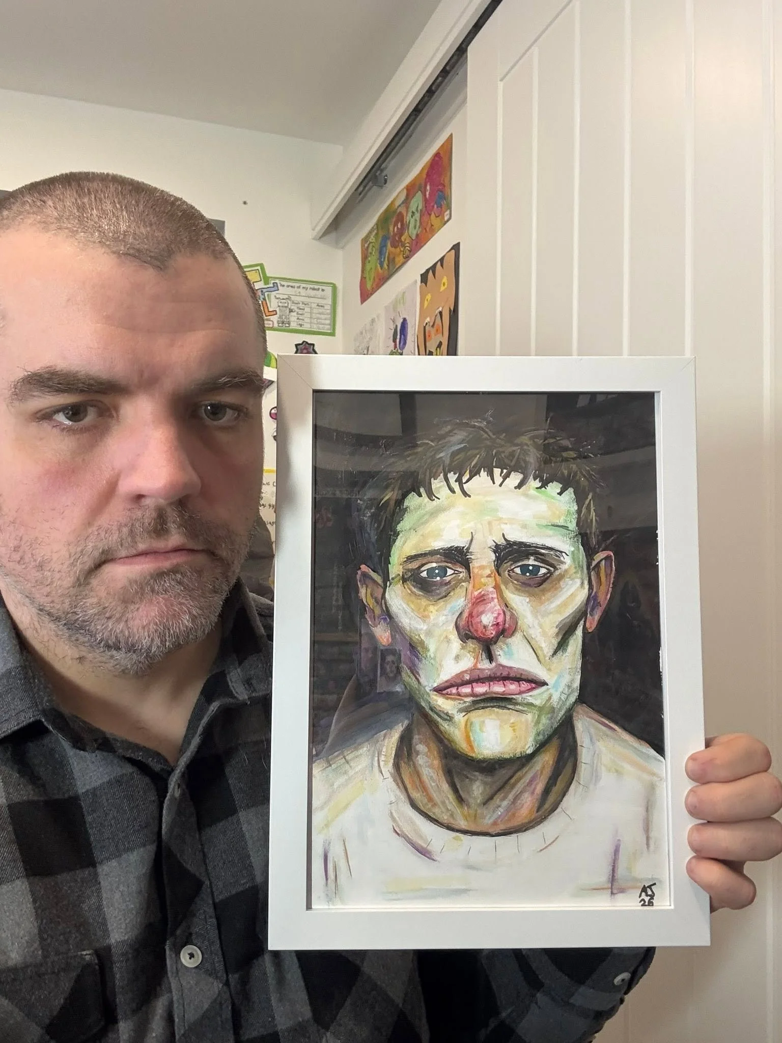 A man with short hair and facial hair holding a framed watercolor portrait of himself, featuring expressive brushstrokes and vibrant colors.