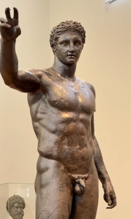 Y aquí, en el corazón de Atenas,
dentro del Museo Arqueológico Nacional,
nos encontramos con una presencia que ha viajado más que cualquiera de nosotros.

Ante nosotros, el Efebo de Anticitera.

Una majestuosa estatua de bronce del siglo IV a. C.,
at
