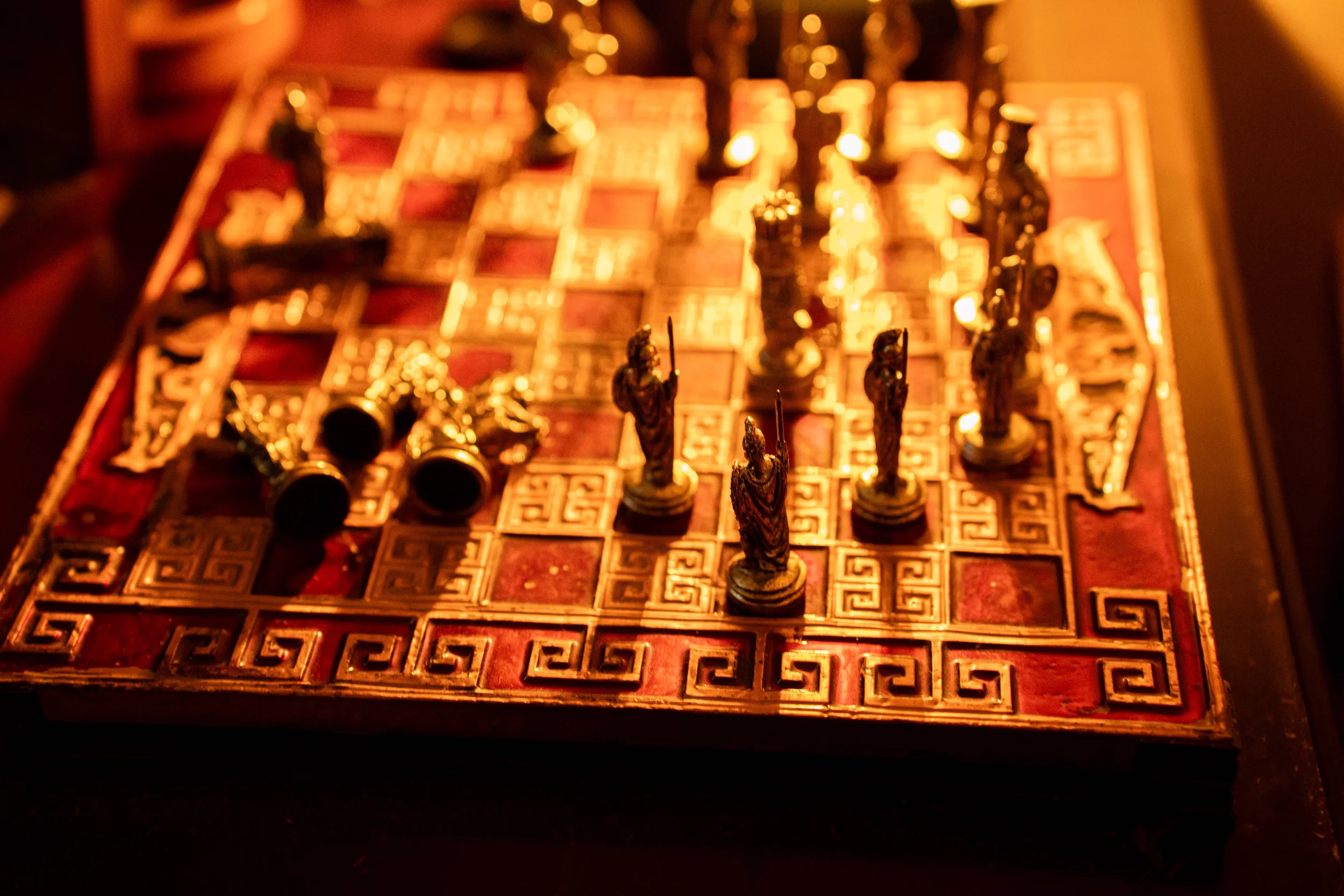 Close-up of a vintage chessboard with intricately carved chess pieces and a geometric pattern on the board, illuminated by warm, dim lighting.