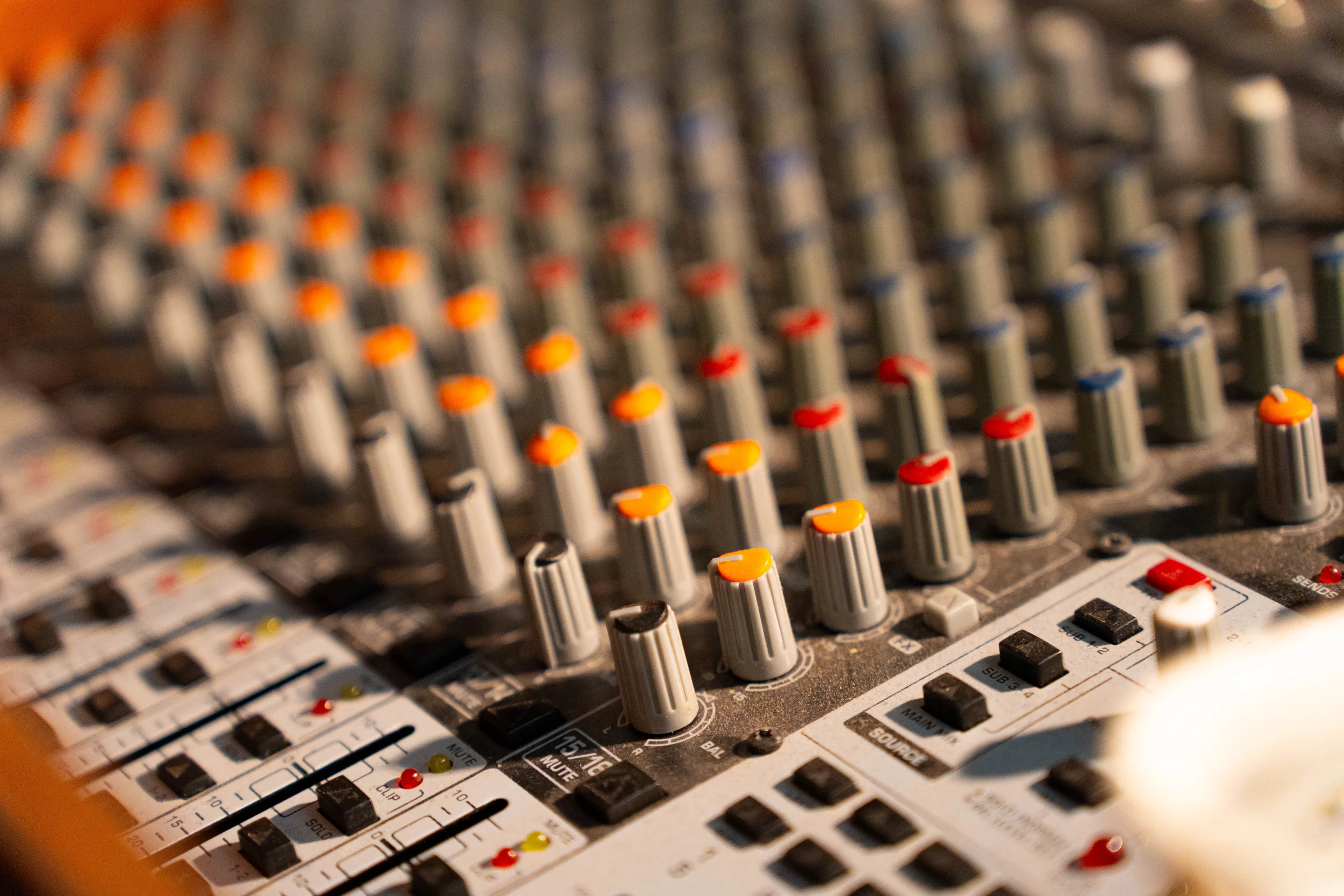 Close-up of an audio mixing console with various sliders, knobs, and buttons.
