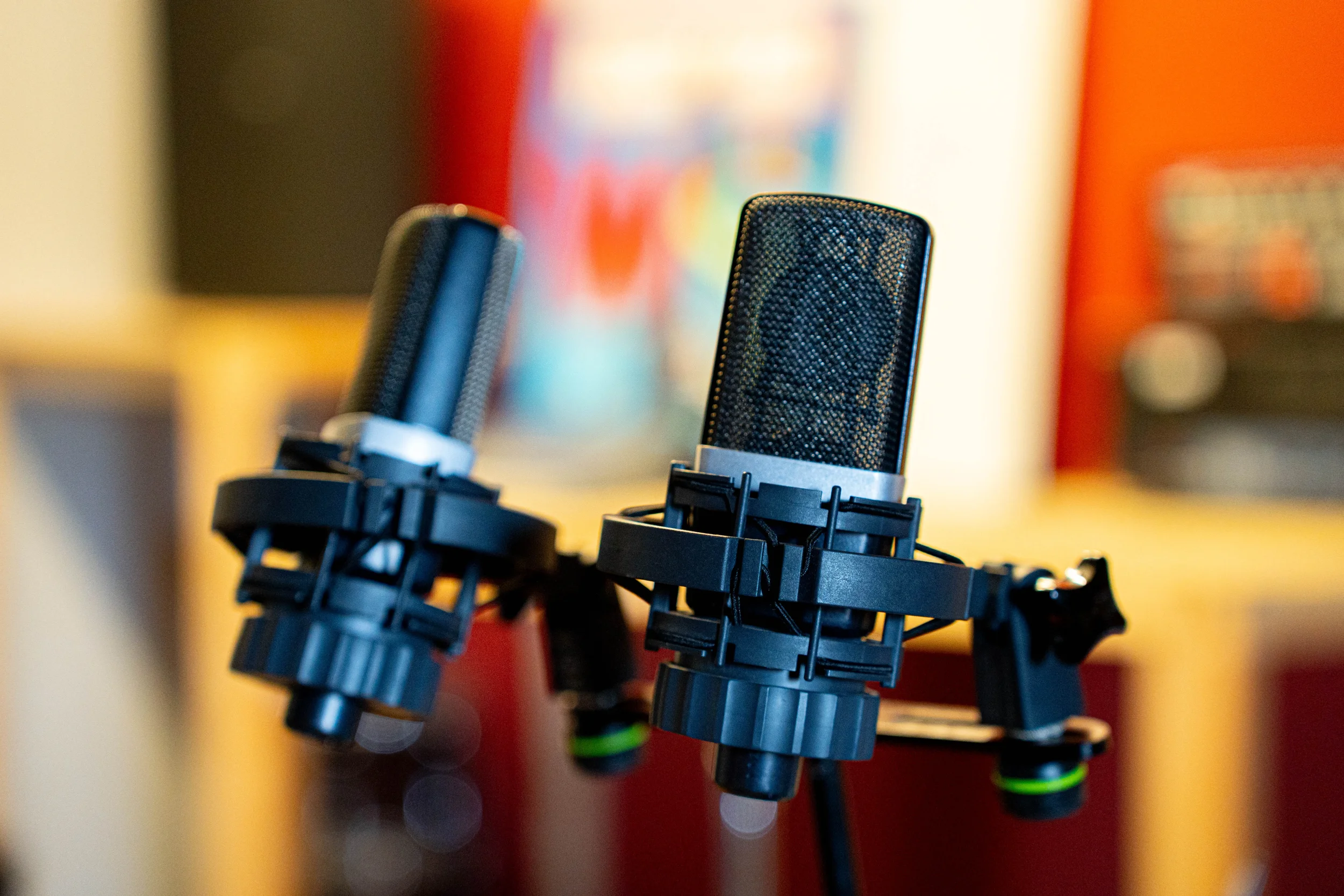 Close-up of three professional studio microphones mounted on adjustable stands, set against a blurred colorful background.