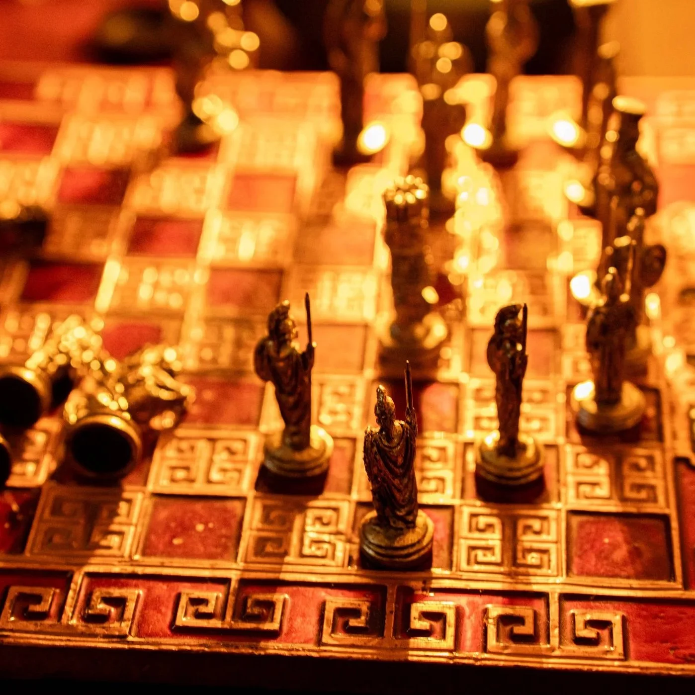 Close-up of chess pieces on a decorative chessboard with an intricate geometric pattern, connected to a game of chess in progress, with blurred background.