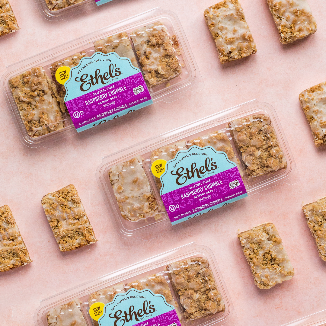 Multiple packages of Ethel's gluten-free raspberry crumble dessert bars, with some bars placed around the packages on a pink background.