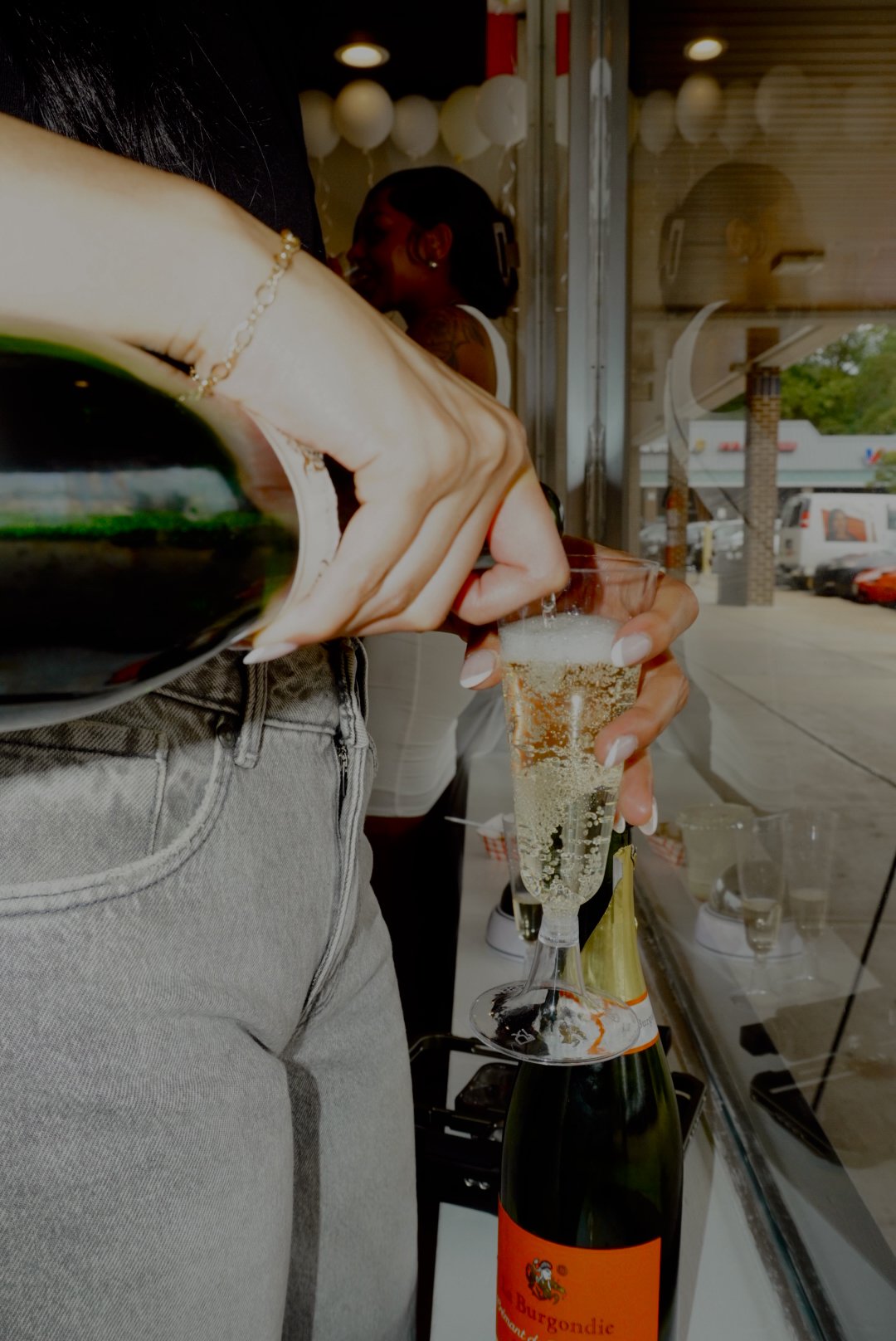 Person holding a champagne flute beside an open bottle of sparkling wine at a restaurant or bar