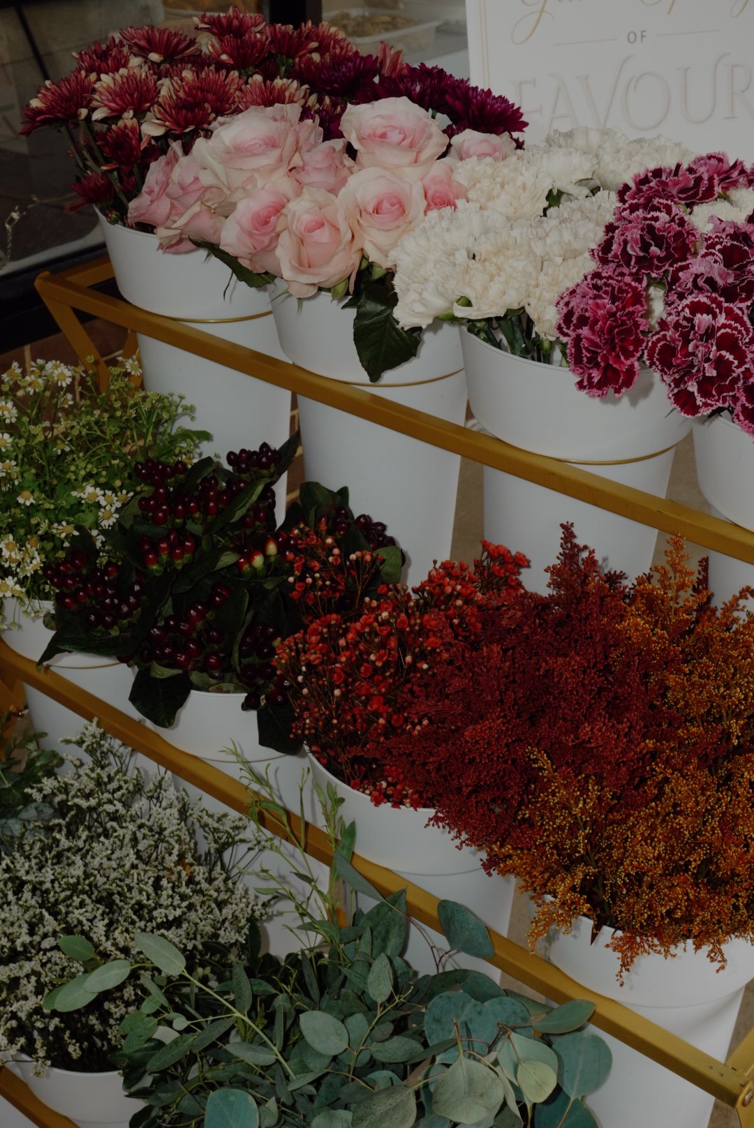Display of fresh pink roses, chrysanthemums, carnations, berries, dried flowers, and eucalyptus in white flower buckets.