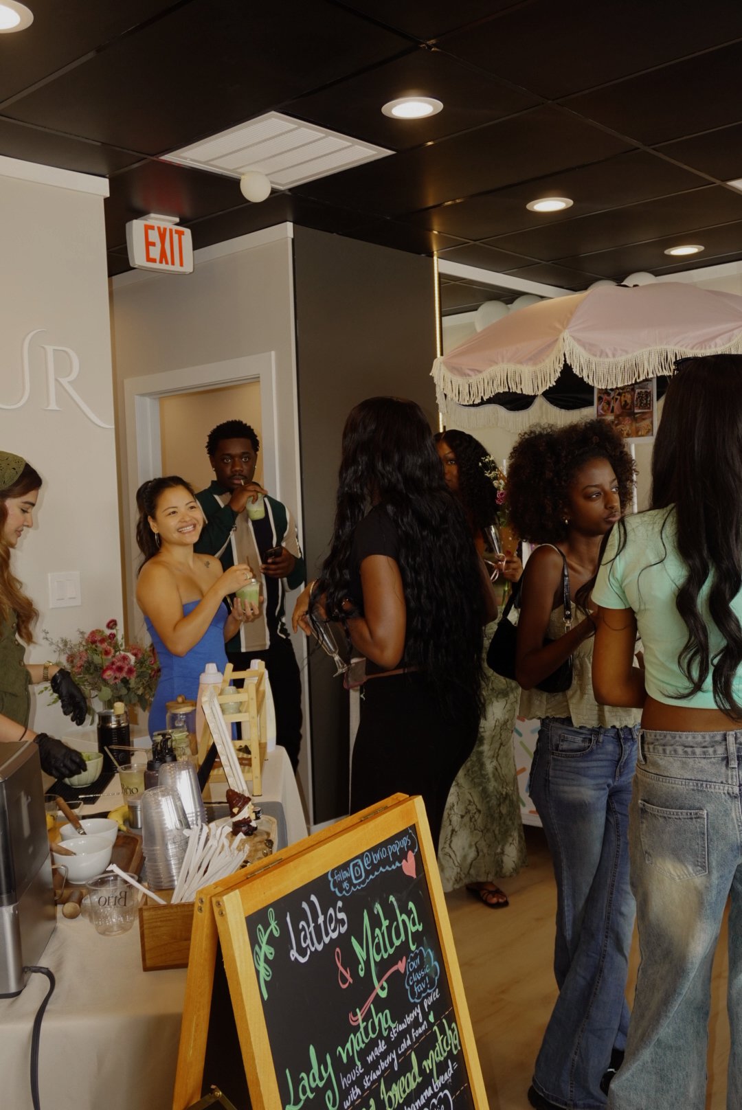 Guests socialize at a pop-up matcha and latte bar with a chalkboard menu and floral canopy.