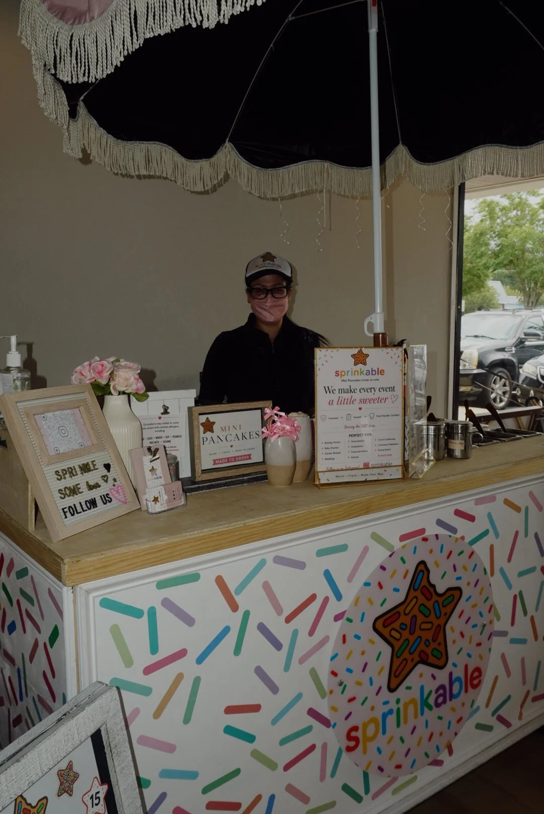Sprinkable mini pancake vendor booth with masked attendant, colorful sprinkle decorations, and event catering signs.