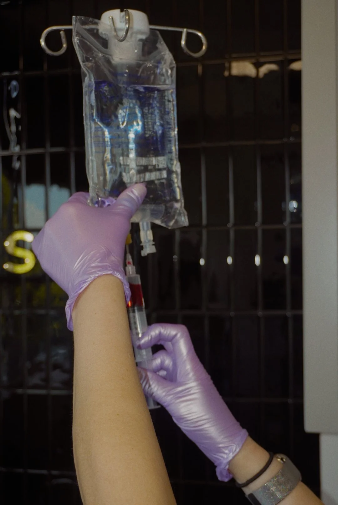 Healthcare worker wearing purple gloves holds an intravenous fluid bag and tubing.