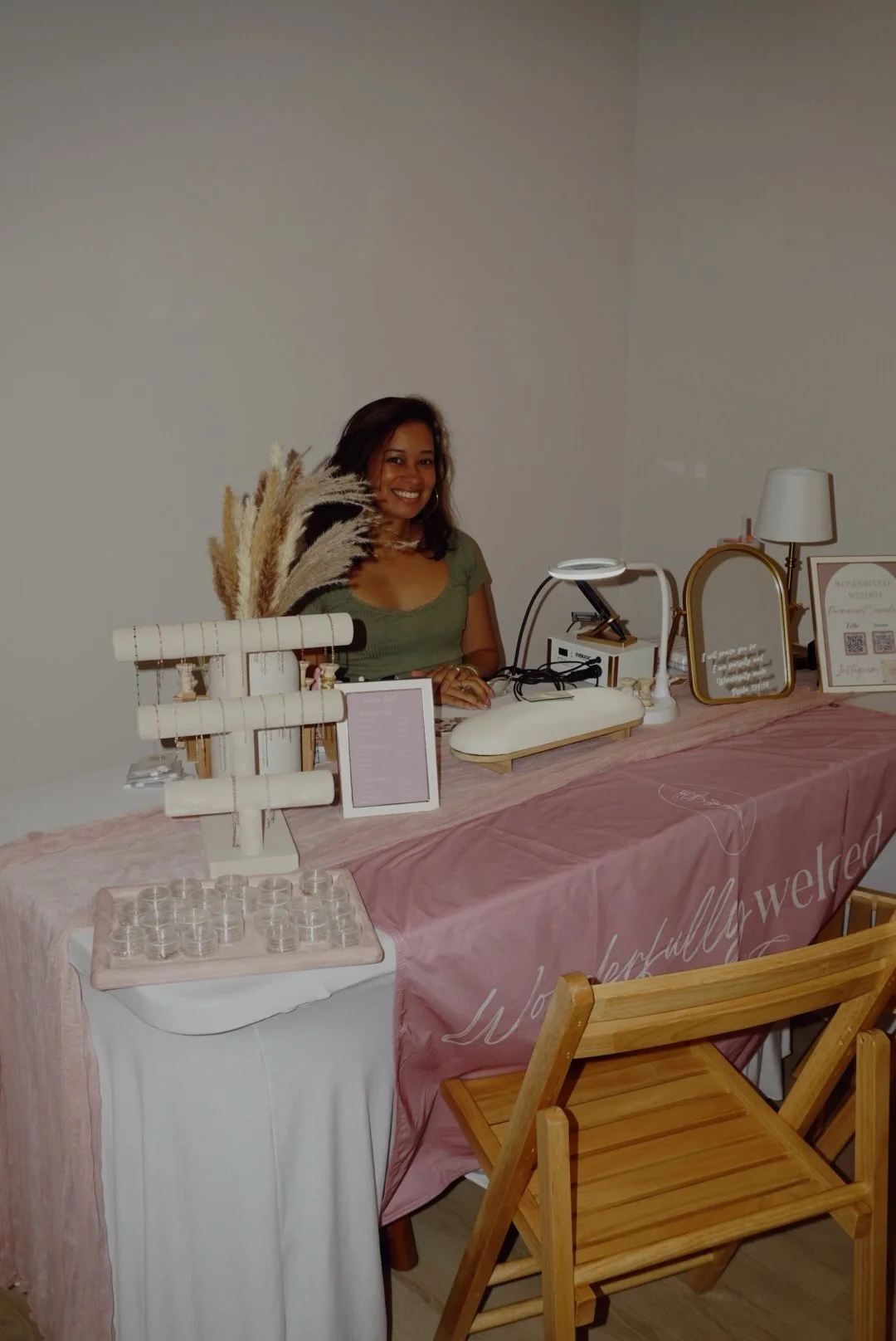 Woman seated behind a decorated jewelry and beverage display table at an indoor event