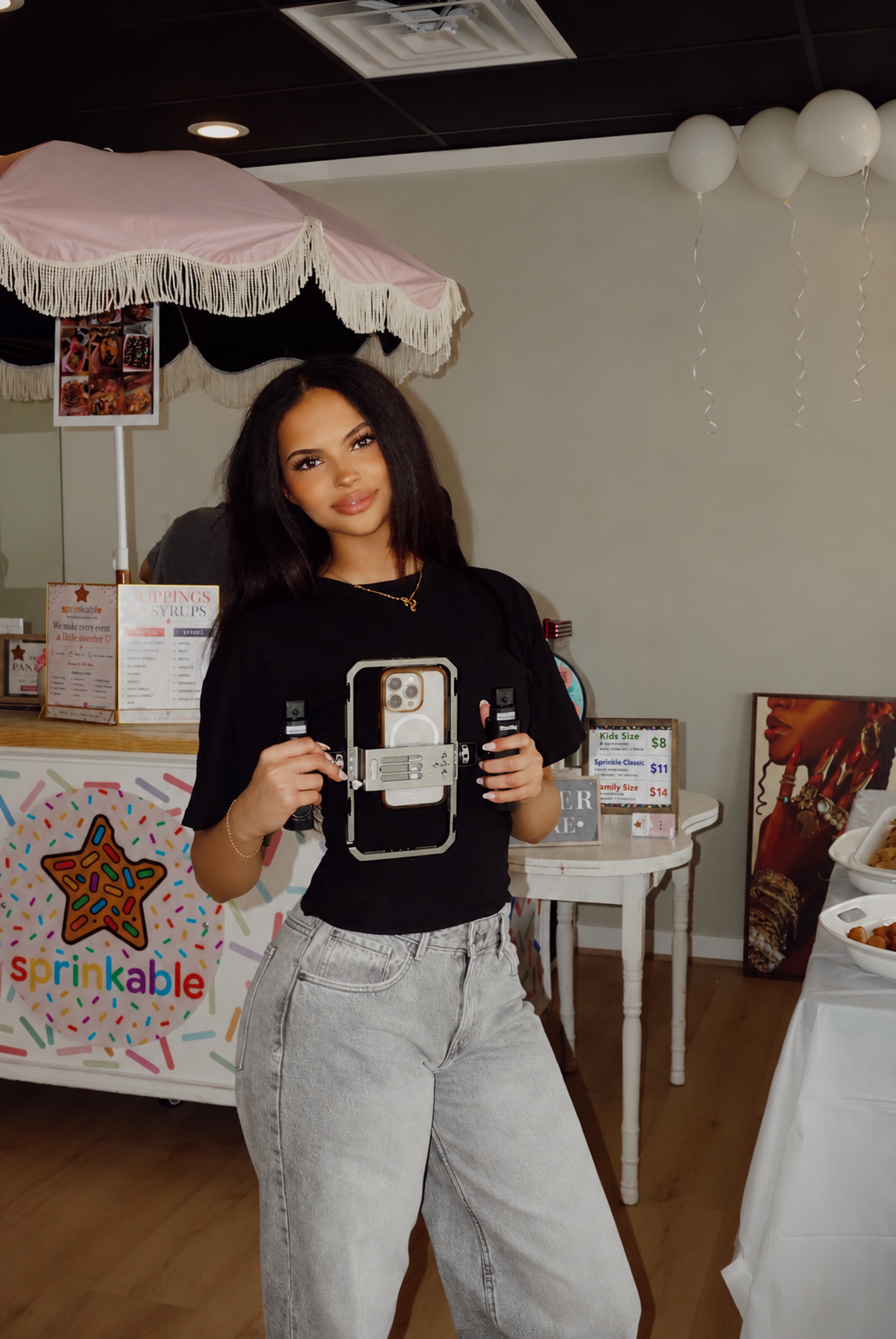 Woman holding a smartphone on a camera rig at a decorated Sprinkable dessert shop