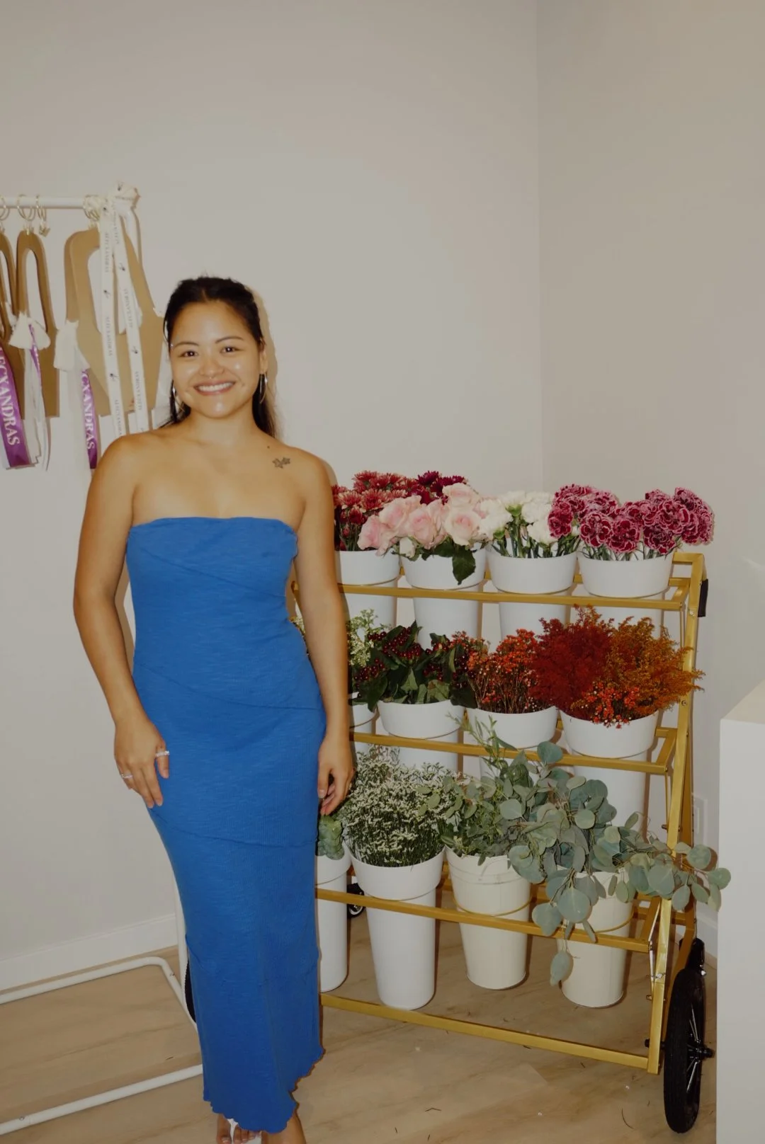 Smiling woman in a blue strapless dress standing beside a flower display cart with colorful bouquets