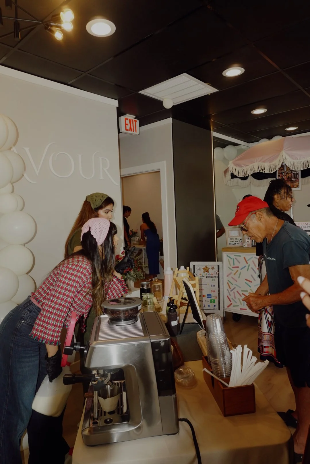 People gathered at a café counter beside an espresso machine and mini pancake stand.