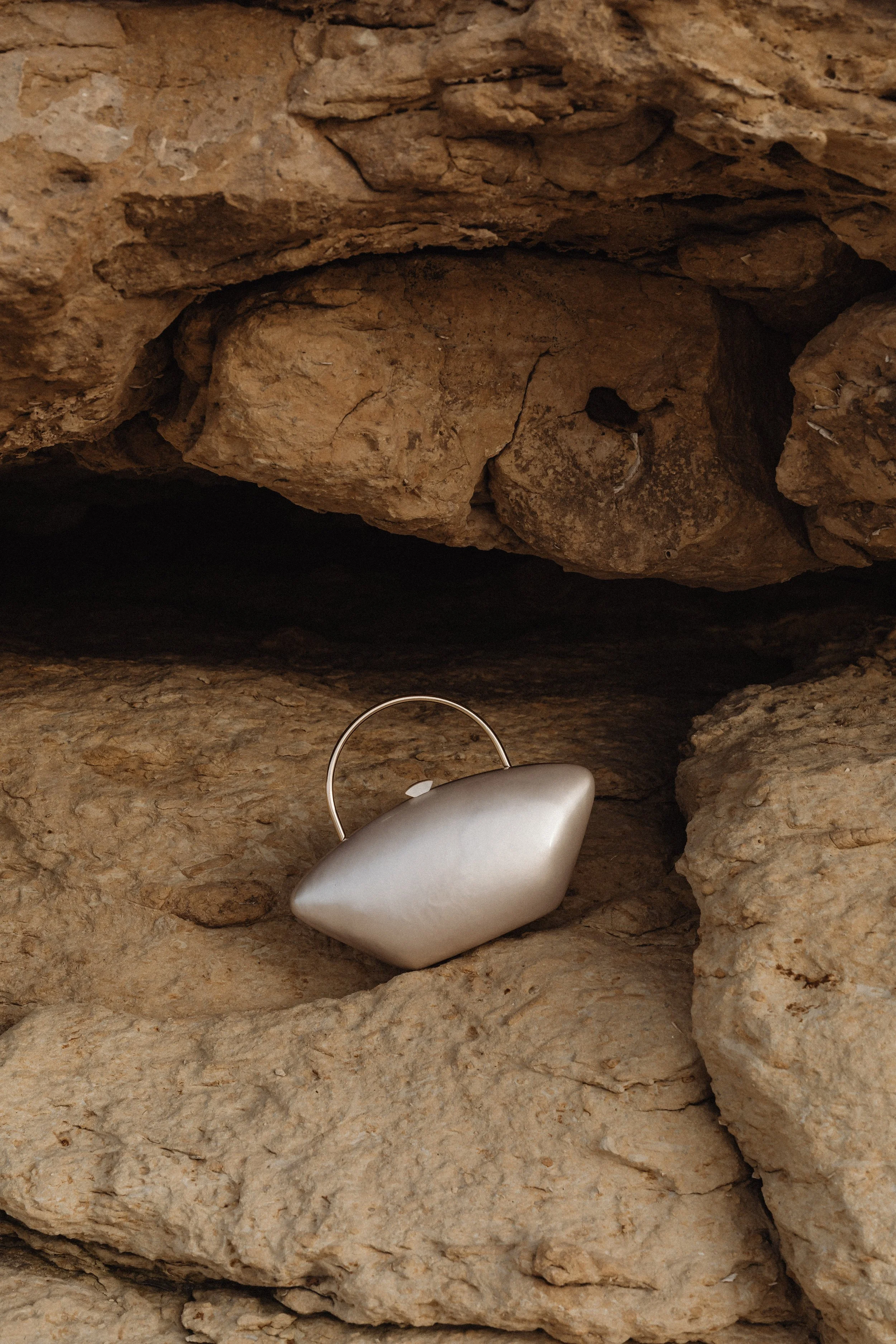 A white modern sculpture resembling a seashell or smooth pebble perched within a small crevice of layered brown rocks.