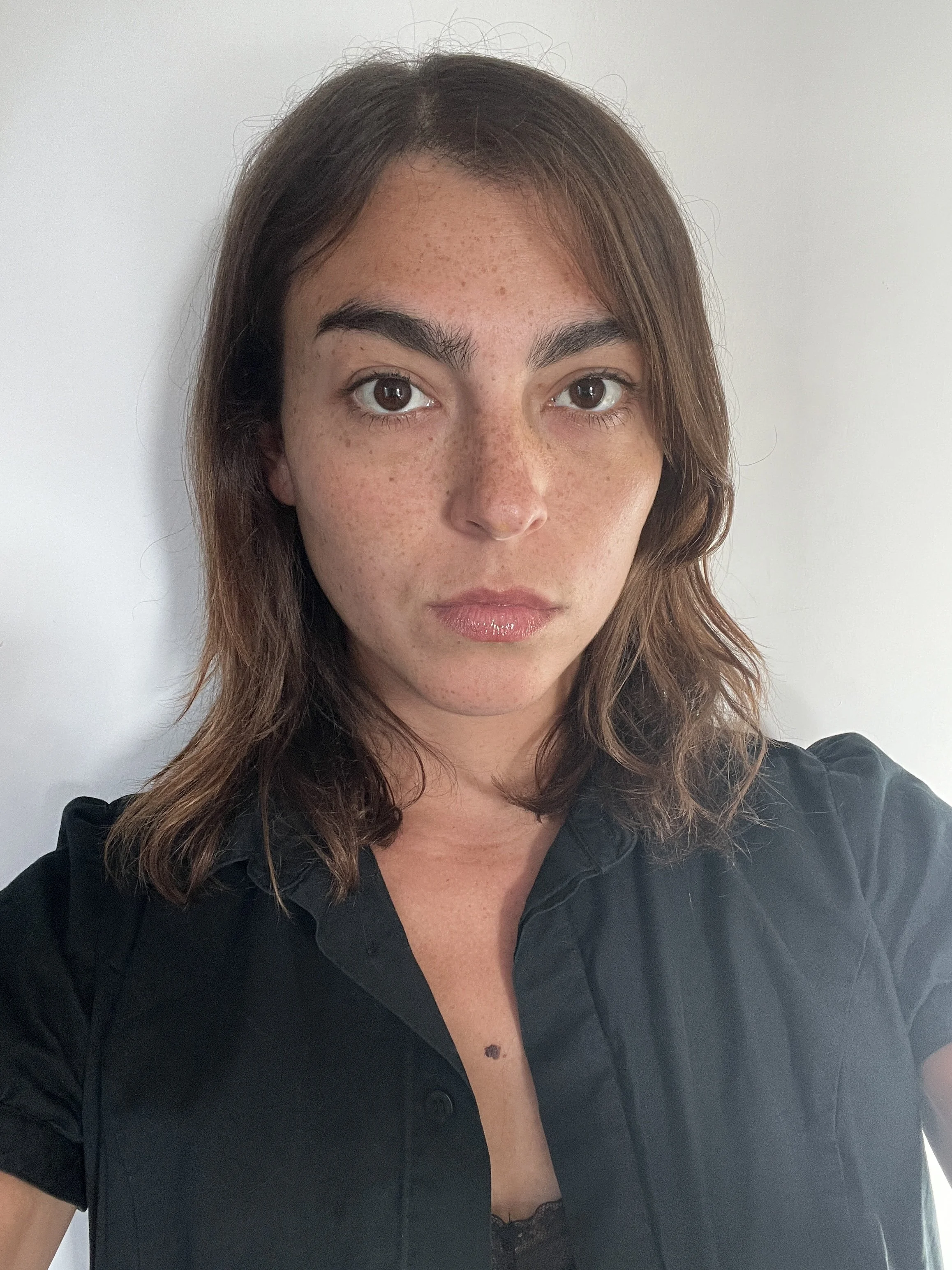 A woman with brown hair and freckles wearing a black shirt, looking at the camera against a plain white background.