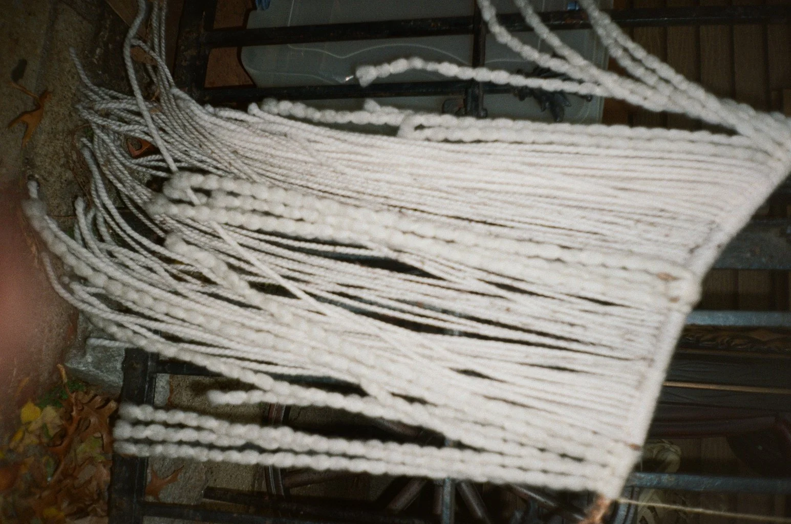 A pile of white ropes arranged on a metal bench outdoors, with some dried leaves on the ground.