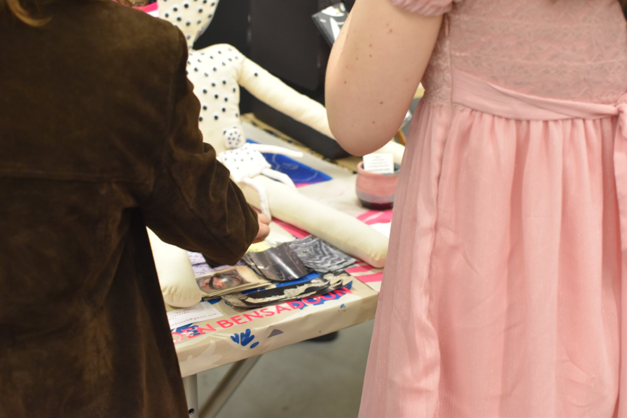 People browsing items at a market stall with a table covered in books and other products.