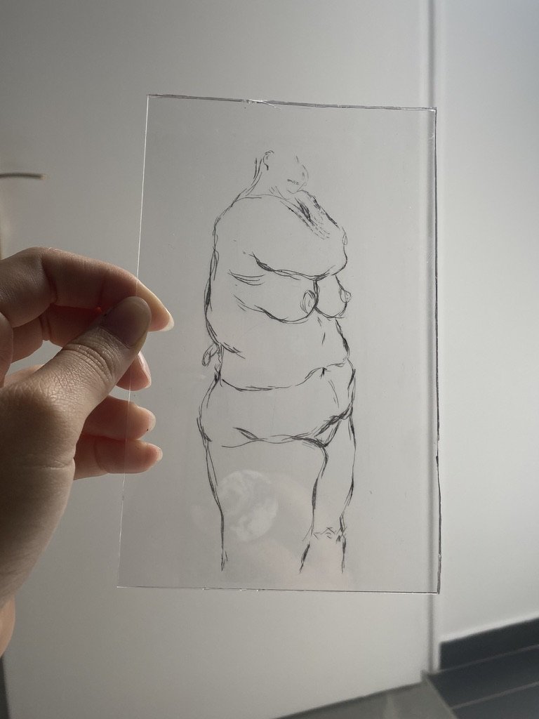 Hand holding a clear glass or acrylic sheet with a black line drawing of a nude stocky woman in minimalistic style.