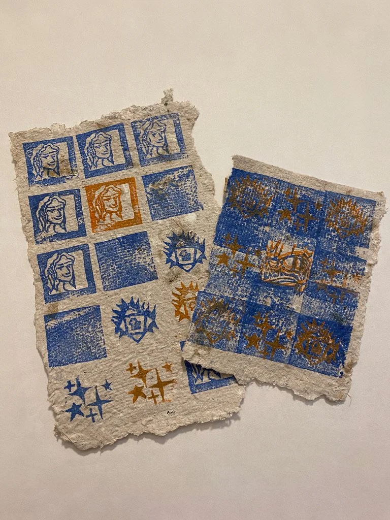 Two torn pieces of textured paper with printed blue and orange symbols, including faces, crosses, stars, and geometric patterns.