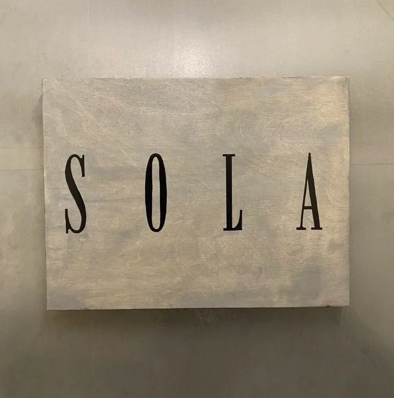 A light-colored wooden box with the word 'SOLA' written in black capital letters.