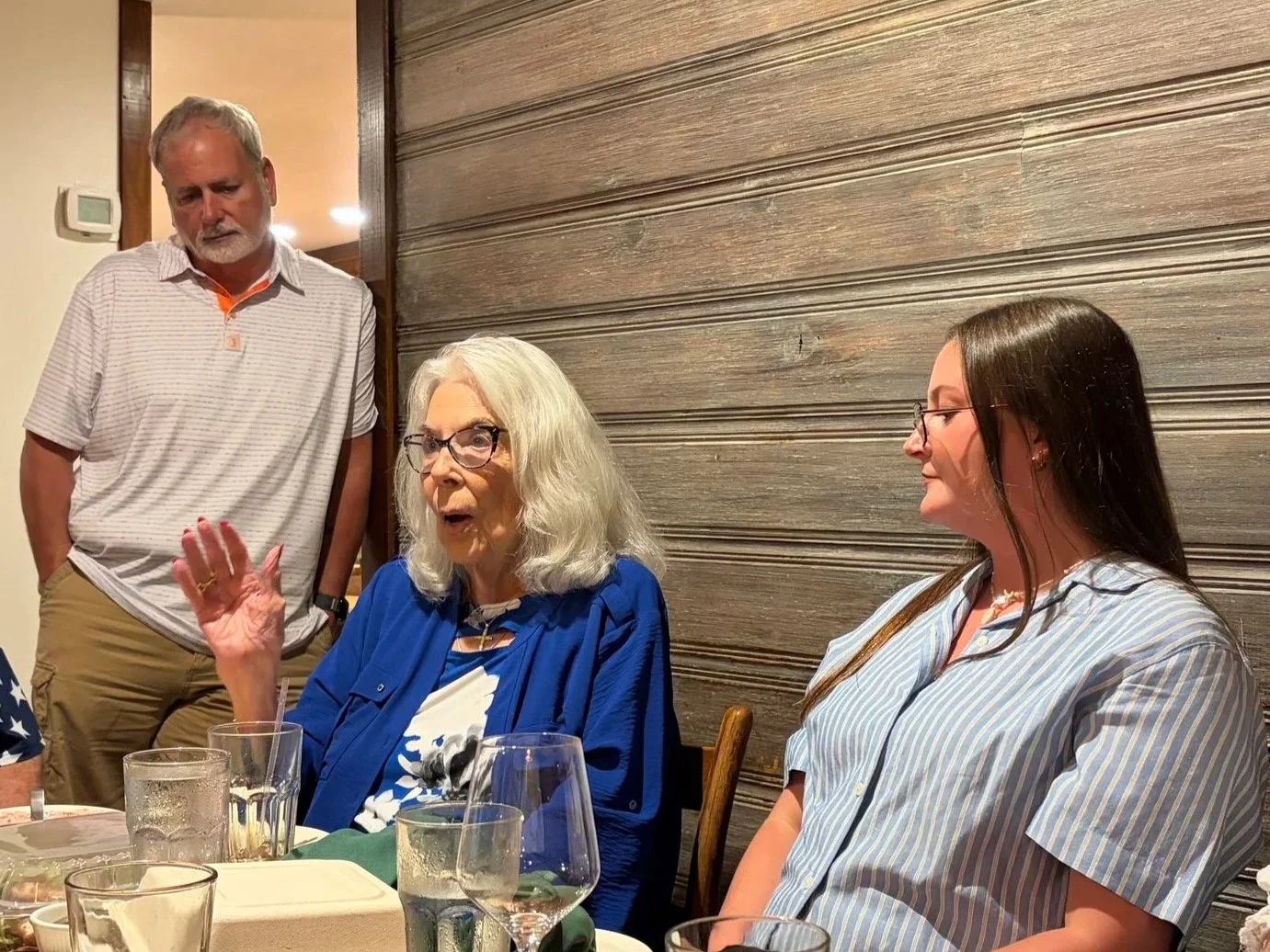 Three adults in conversation over dinner, with an older woman speaking.