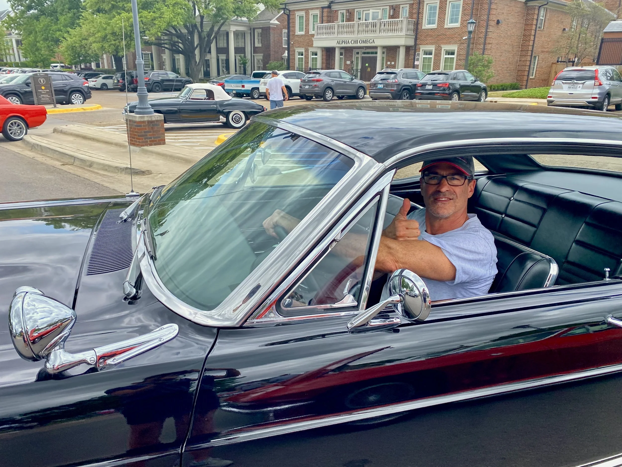 Adult 50+ seated in a vintage car giving a thumbs-up.