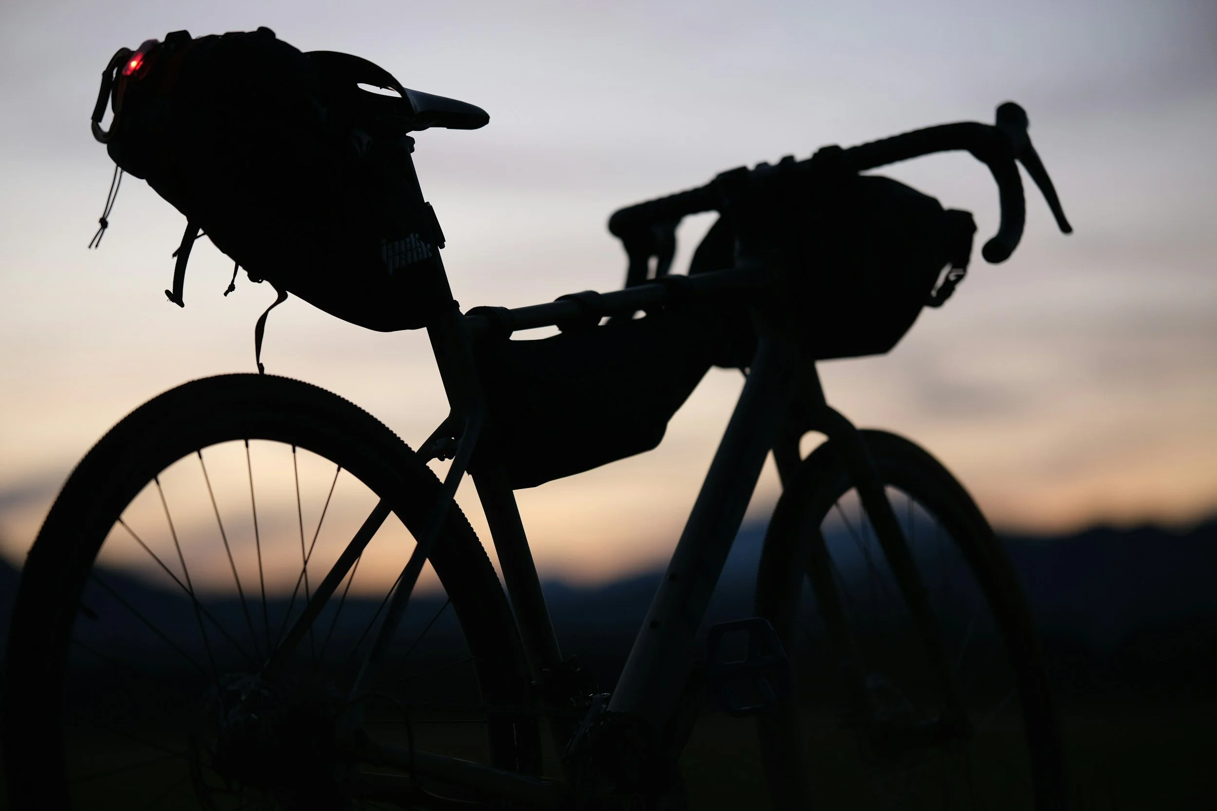 Silhouette of a bicycle with bikepacking bags against a sunset sky.