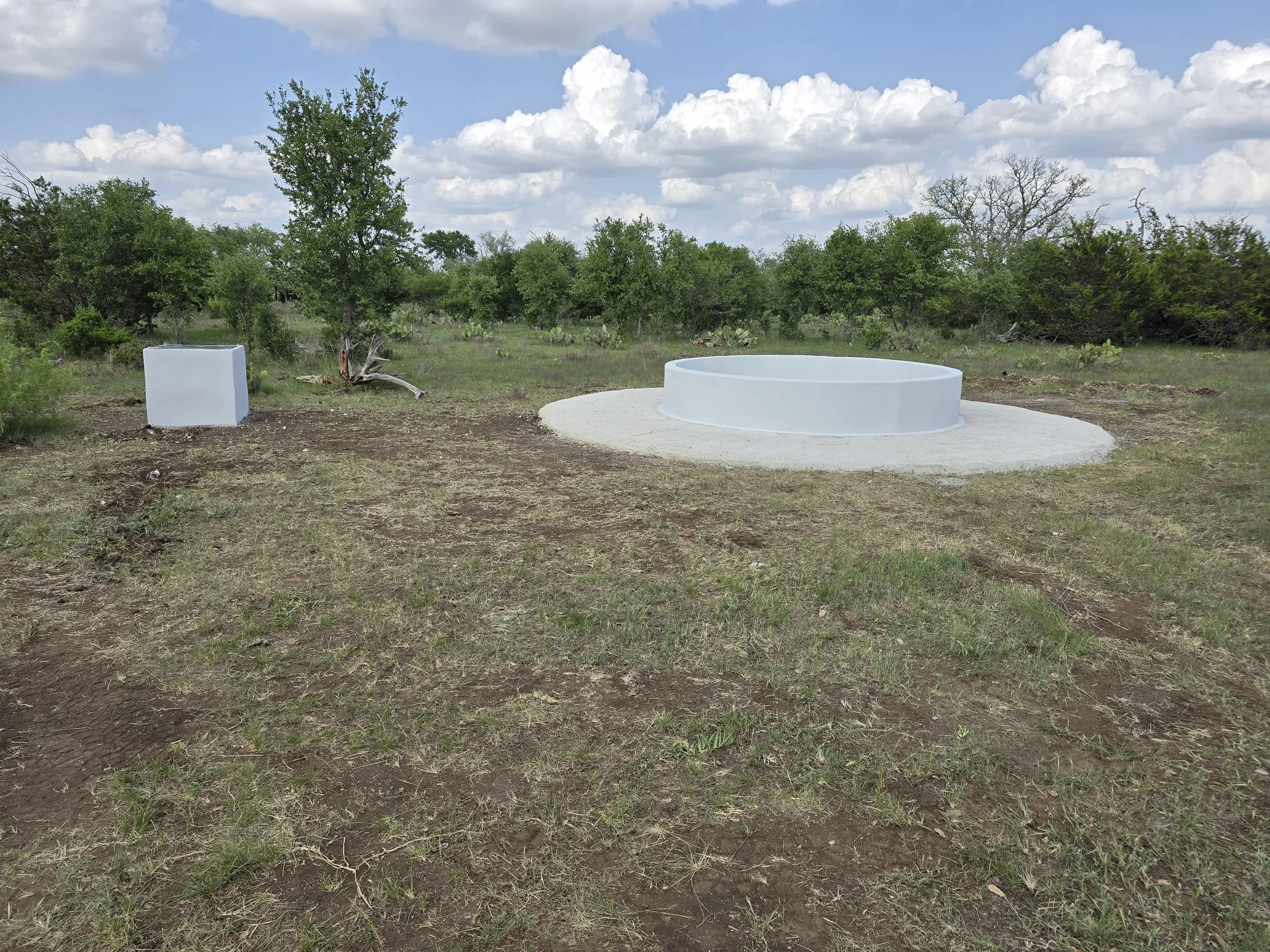 A large white circular structure outdoors on a grassy area with trees and clouds in the background.