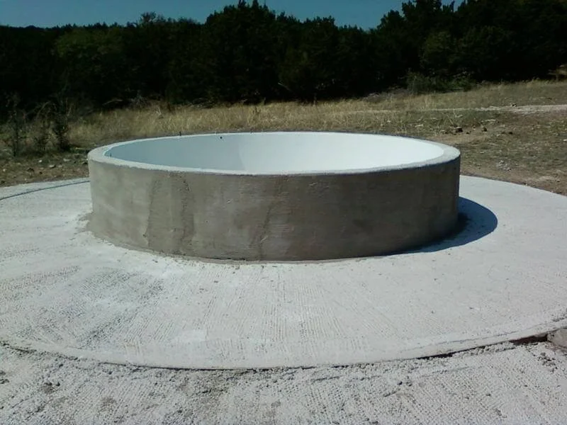 Concrete circular structure with an interior lined with white material, set on a flat concrete surface in an outdoor area with grass and trees in the background.