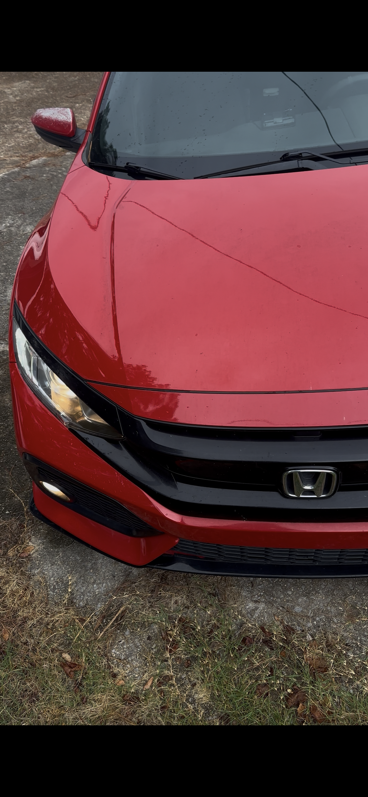 Close-up of the front part of a red Honda car parked on a patch of grass and dirt.