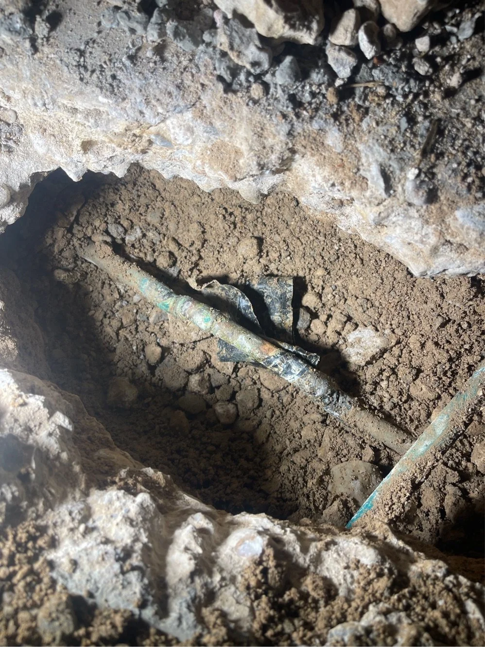 Close-up of a small excavation with dirt and buried pipes or cables.