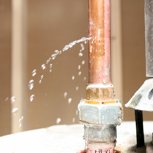 Close-up of a water pipe with water spraying out of a crack in the pipe.
