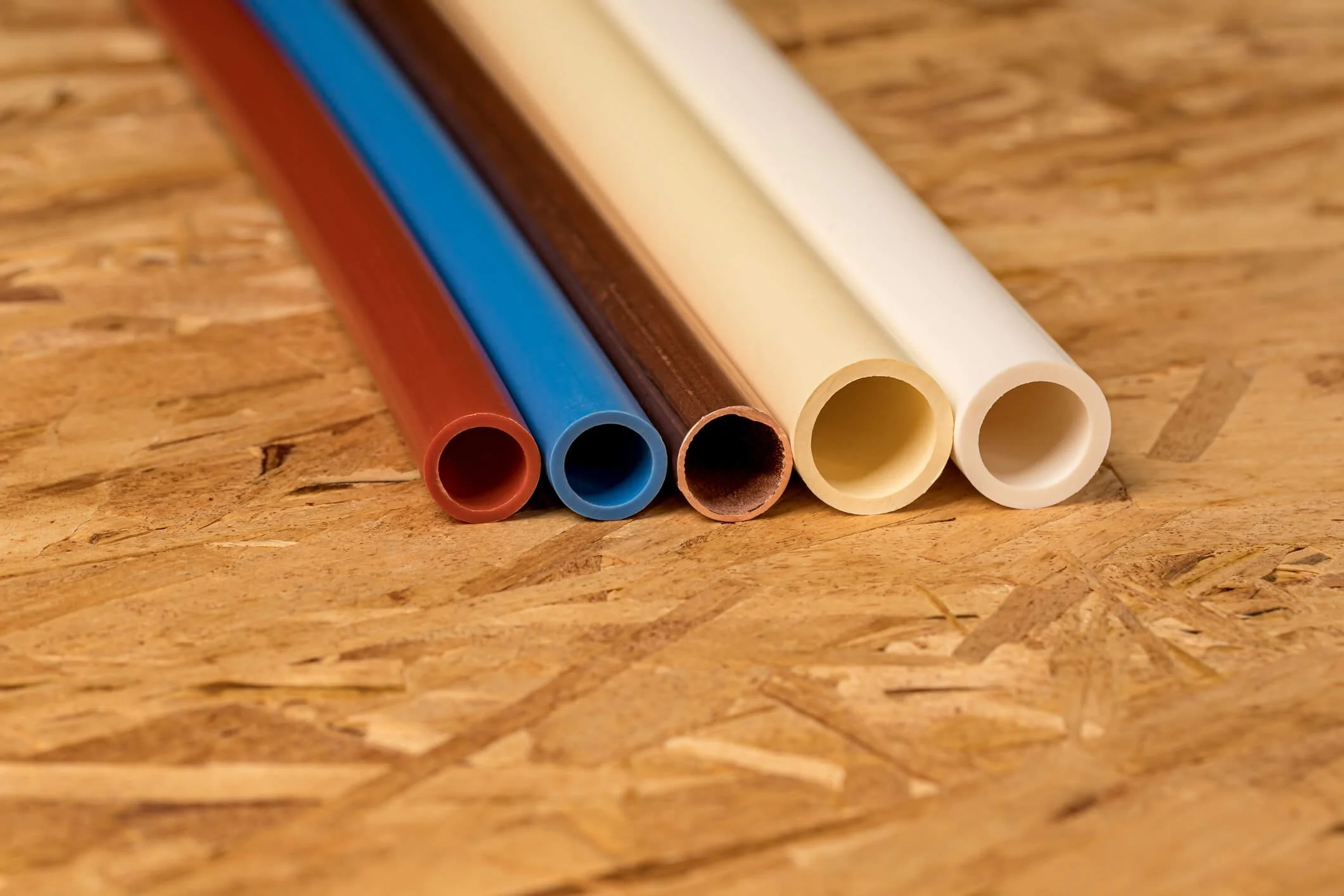Close-up of five colorful plastic straws on a wooden surface, from red to white.