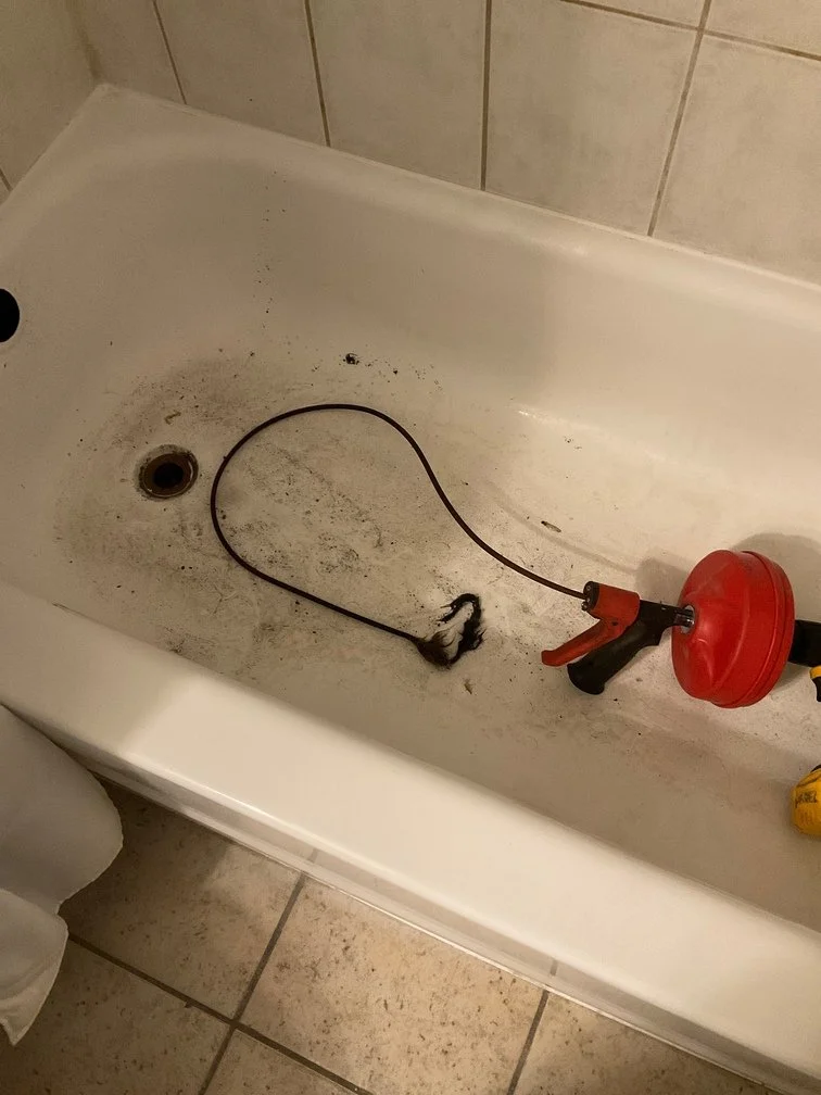 Dirty bathtub with a clogged drain, containing a drain snake and a glue gun.
