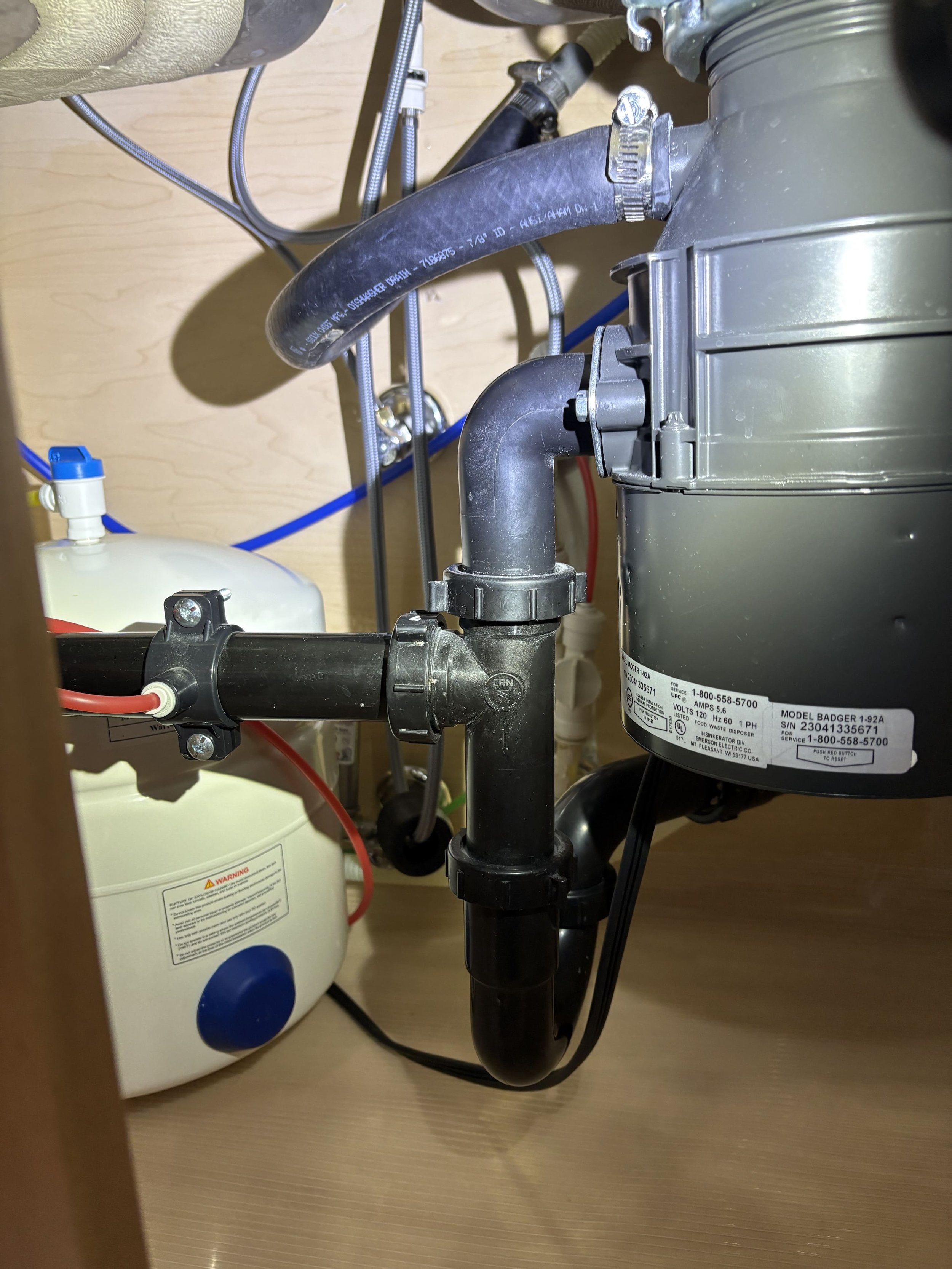 Close-up of plumbing under a sink showing black pipes, a water filter, and connections.