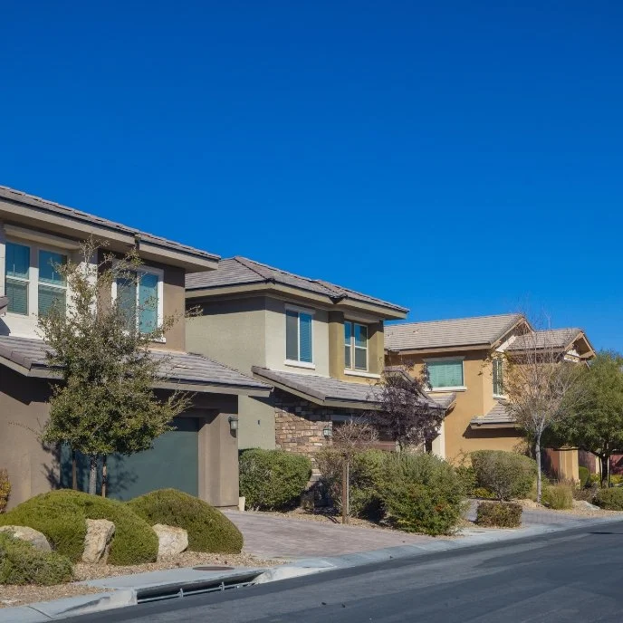 Row of modern suburban houses with landscaped front yards under a clear blue sky.