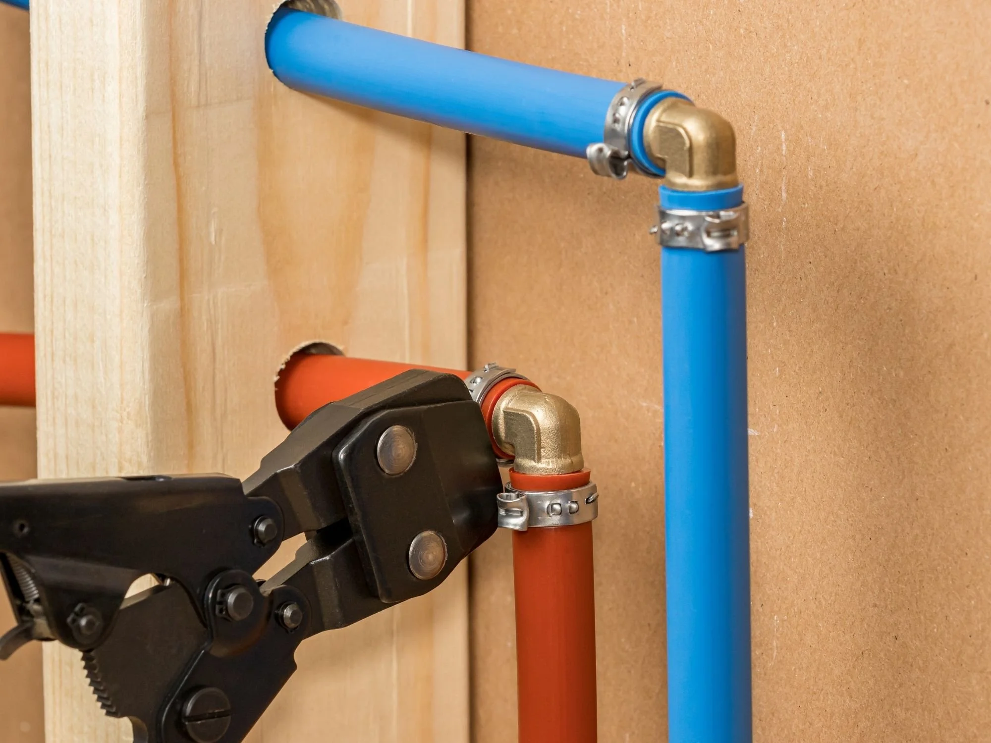 A robotic arm working with plumbing pipes, connecting two pipes, one orange and one blue, on a wooden wall with multiple holes.
