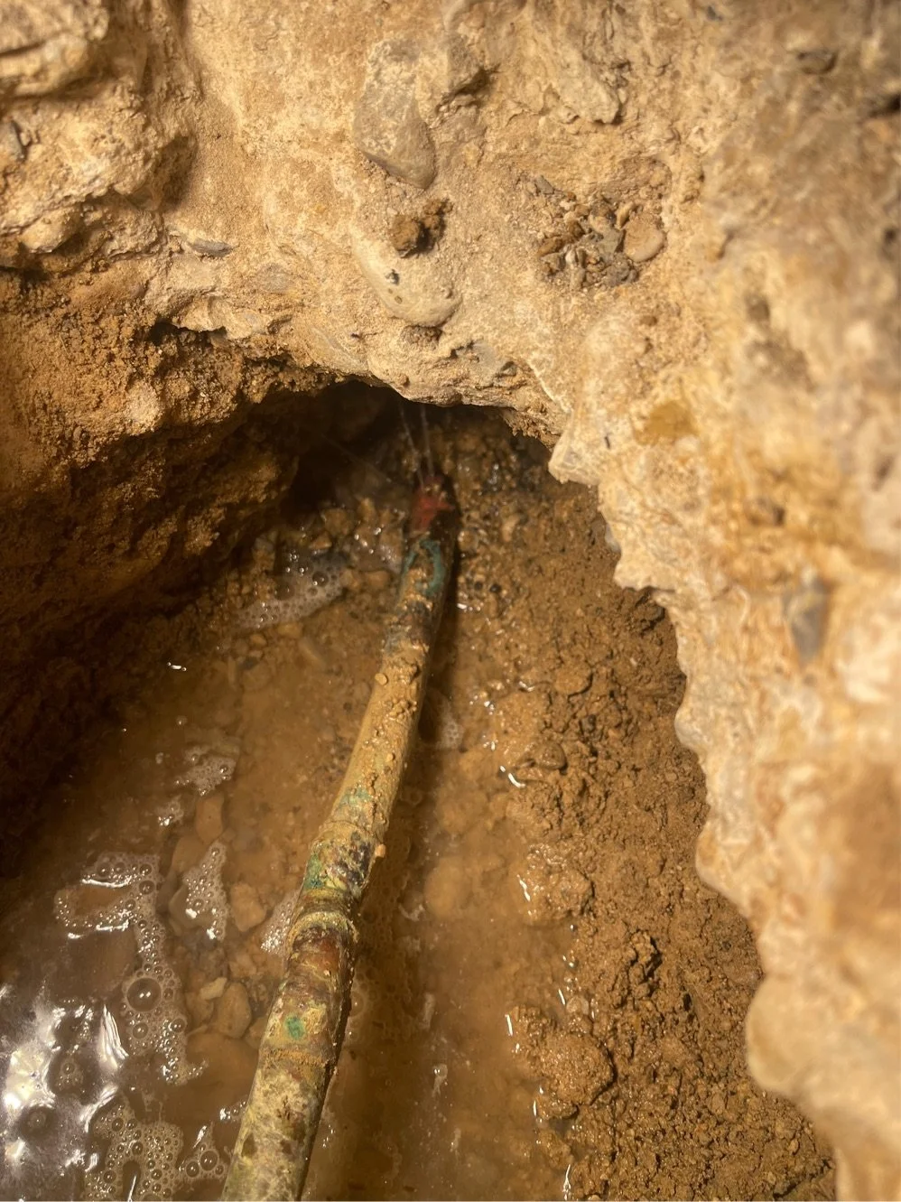 Close-up of a rusty pipe in a small, muddy excavation or repair site.
