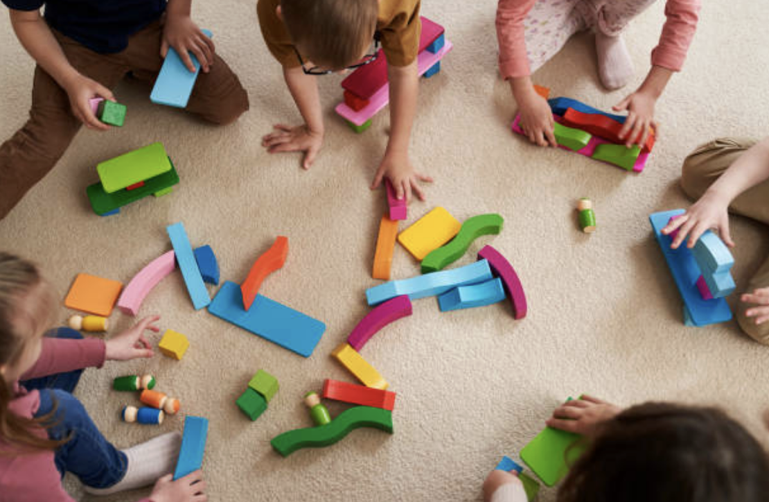 Children playing with colorful wooden building blocks on a beige carpet.